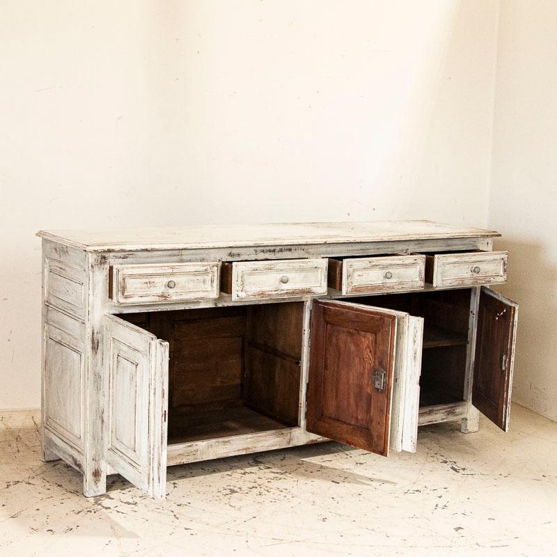 It is a challenge to find a long sideboard, so discovering one this size is a special find. The paneled drawers, doors and sides add to the clean lines of the buffet. The newer white paint has been distressed, adding both dimension and character to