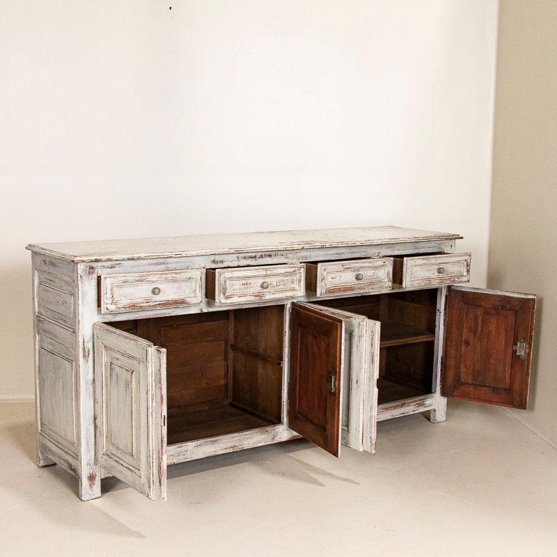 It is a challenge to find a long sideboard, so discovering one this size is a special find. The paneled drawers, doors and sides add to the clean lines of the buffet. The newer white paint has been distressed, adding both dimension and character to