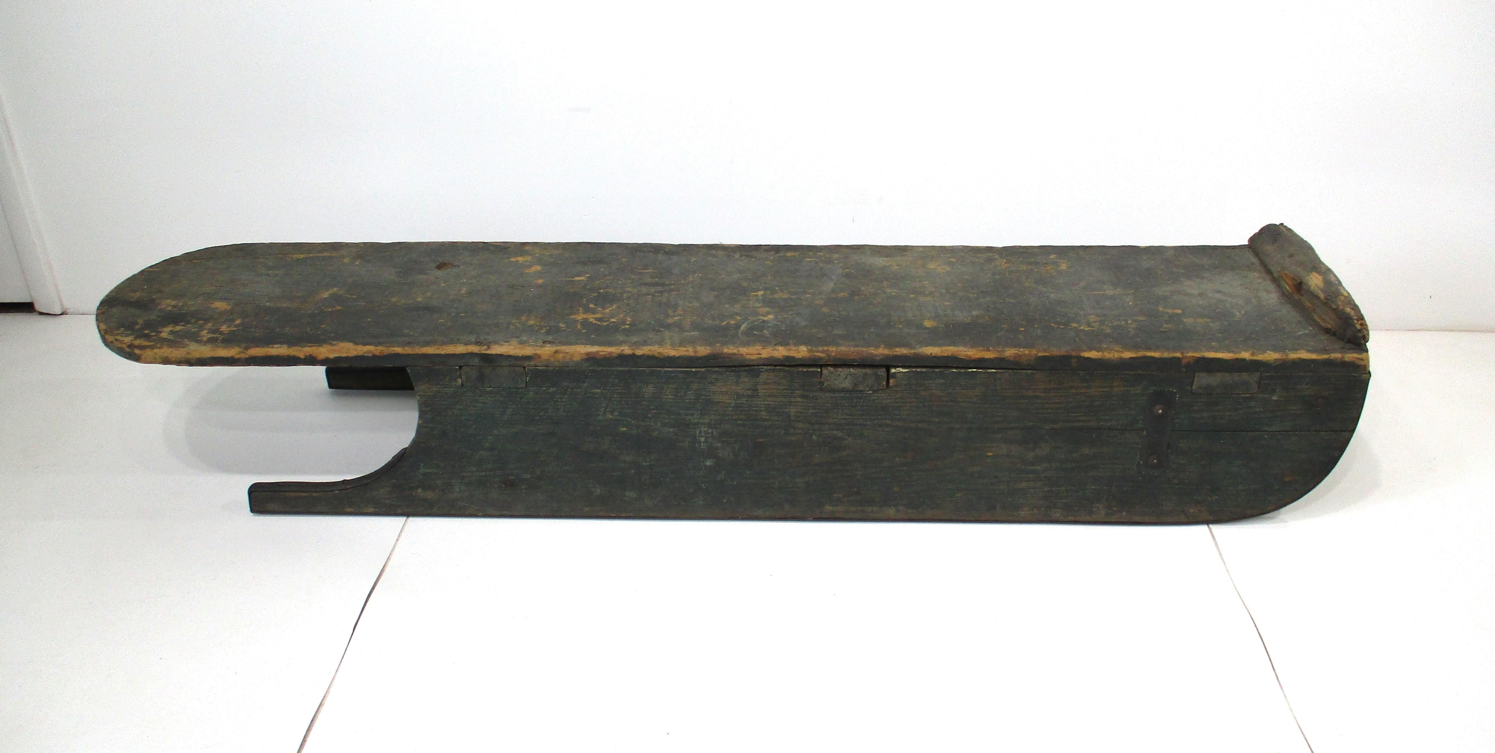Slitta o slittino da ghiaccio o da neve in legno in stile arte popolare, con vernice verde scuro ben usurata e guide in metallo. Questo pezzo presenta una patina eccezionale che dimostra la sua età e il suo utilizzo, con tutti i legni e i metalli