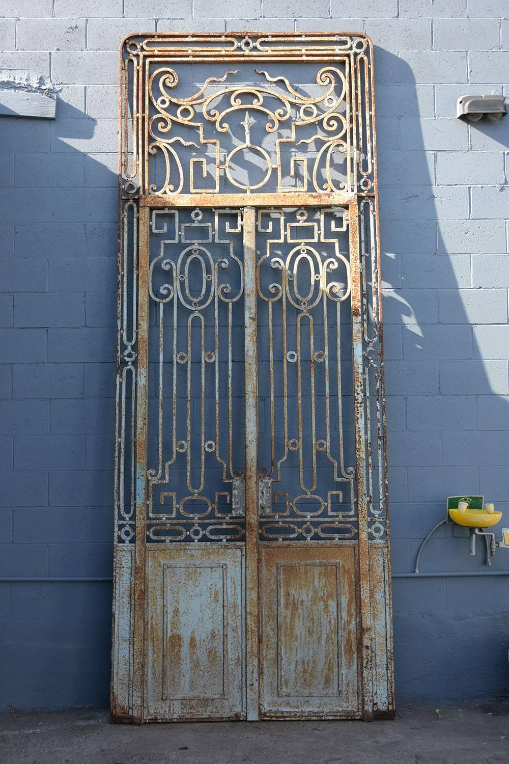 This stunning Regency-style wrought iron gate dates to around the 1850s. The tall gate has two smaller, usable doors and a decorative transom above. Decorating the doors are scroll and geometric designs. Accenting the design of the gate is the