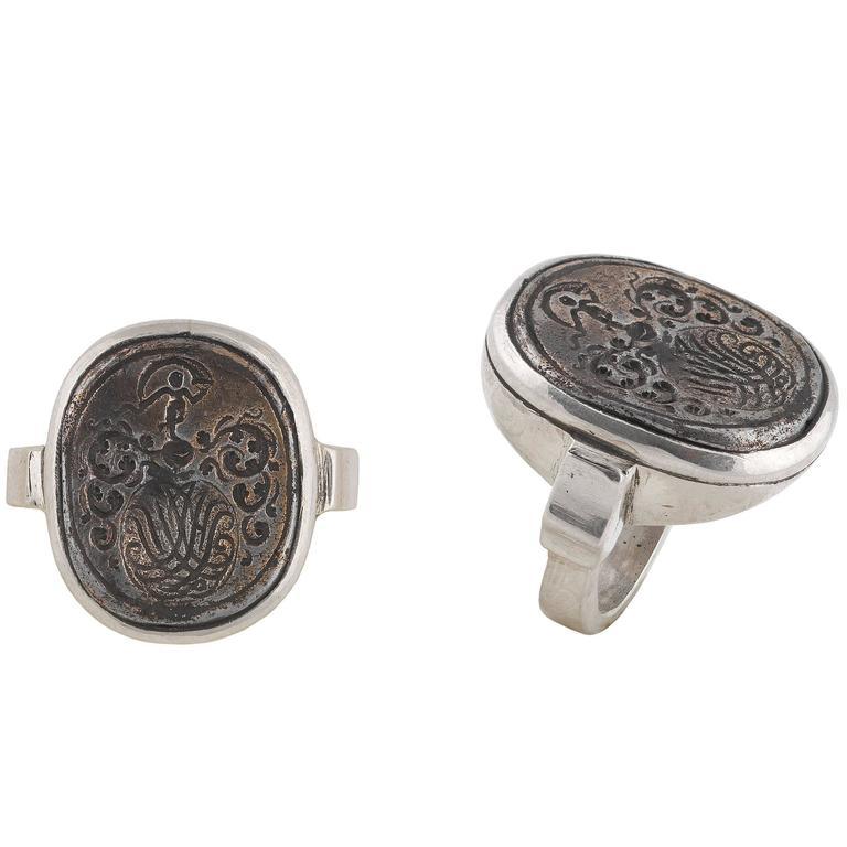 Centrally set with a plaque with with traces of gilding engraved to depict a monogram surmounted and enclosed by a floral decoration, at the top a dancing figure with a ribbon. 

Mounted in silver.

The top 26 mm high 21 mm wide

Finger size: 7