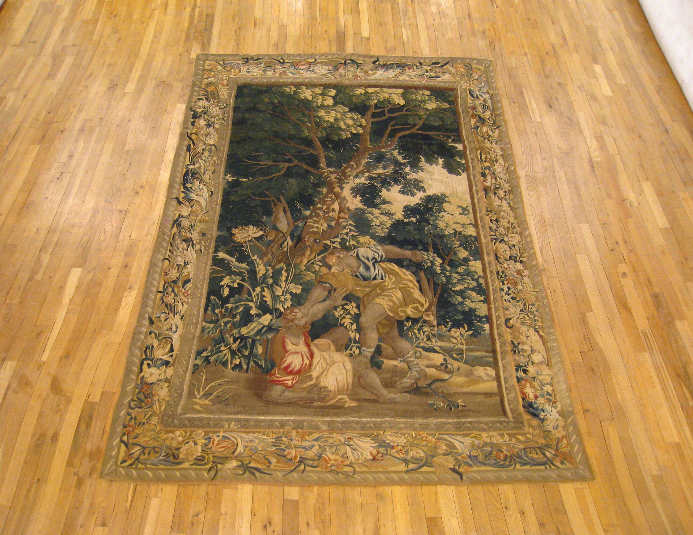 An antique late 17th century Flemish Biblical tapestry, size: 9'5 H x 6'5 W, envisioning the Old Testament Biblical conflict between Cain and Able, with Cain pushing his brother to the ground in a forest setting. Enclosed within a scrolling foliate