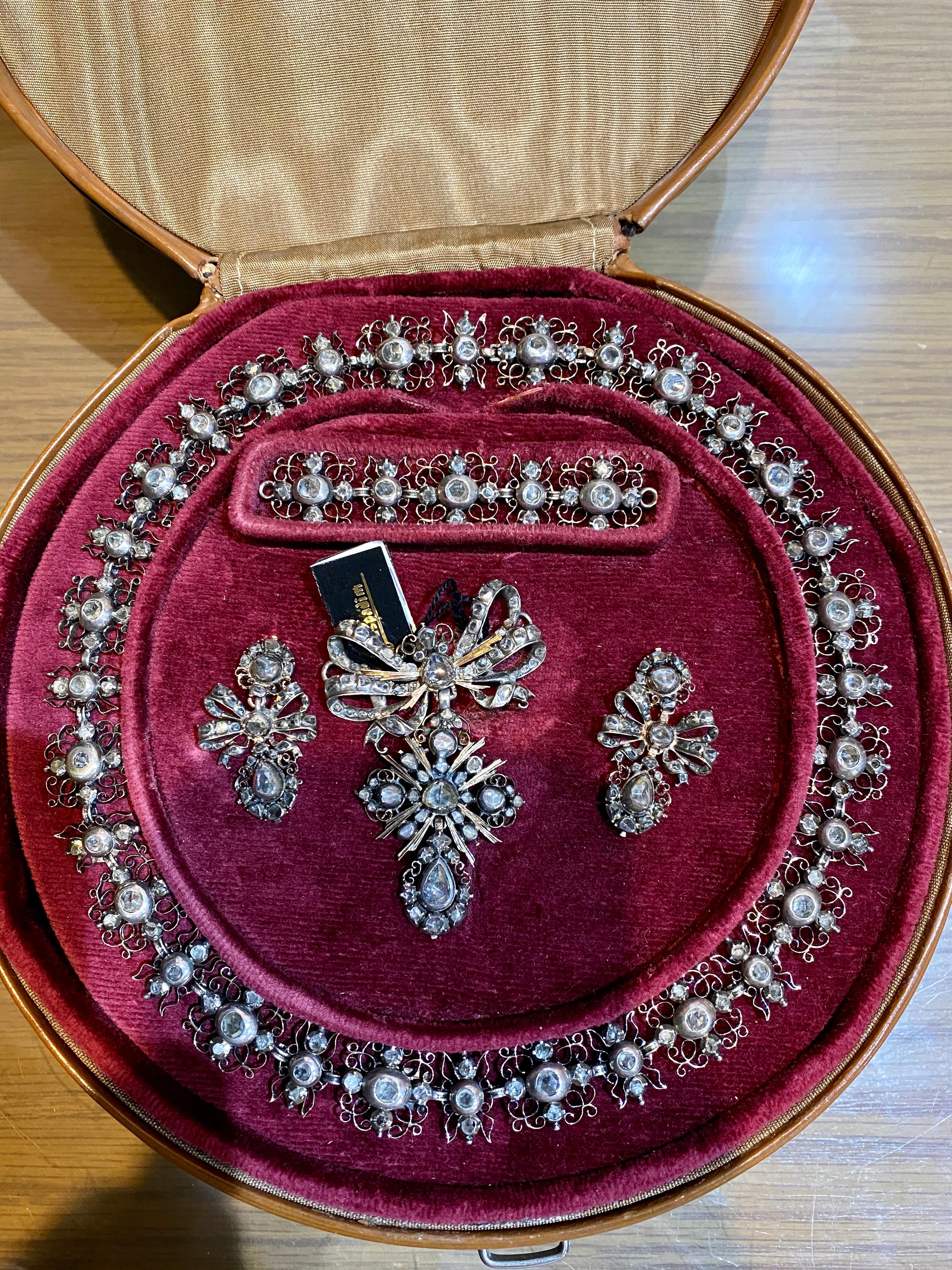 An important late 17th to early 18th century diamond demi-parure in silver and gold, Portuguese, cased. Comprising of a brooch/pendant, a pair of earrings and a necklace, the whole set is embellished throughout with rose-cut diamonds in closed-back