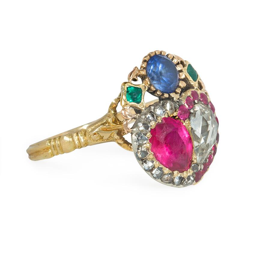 An antique Georgian ring in the form of a double heart comprised of an opposed pear-shaped rose-cut diamond and a ruby in corresponding surrounds and surmounted by an openwork wreath set with a sapphire flanked by emeralds, in 18k gold.

Face-up