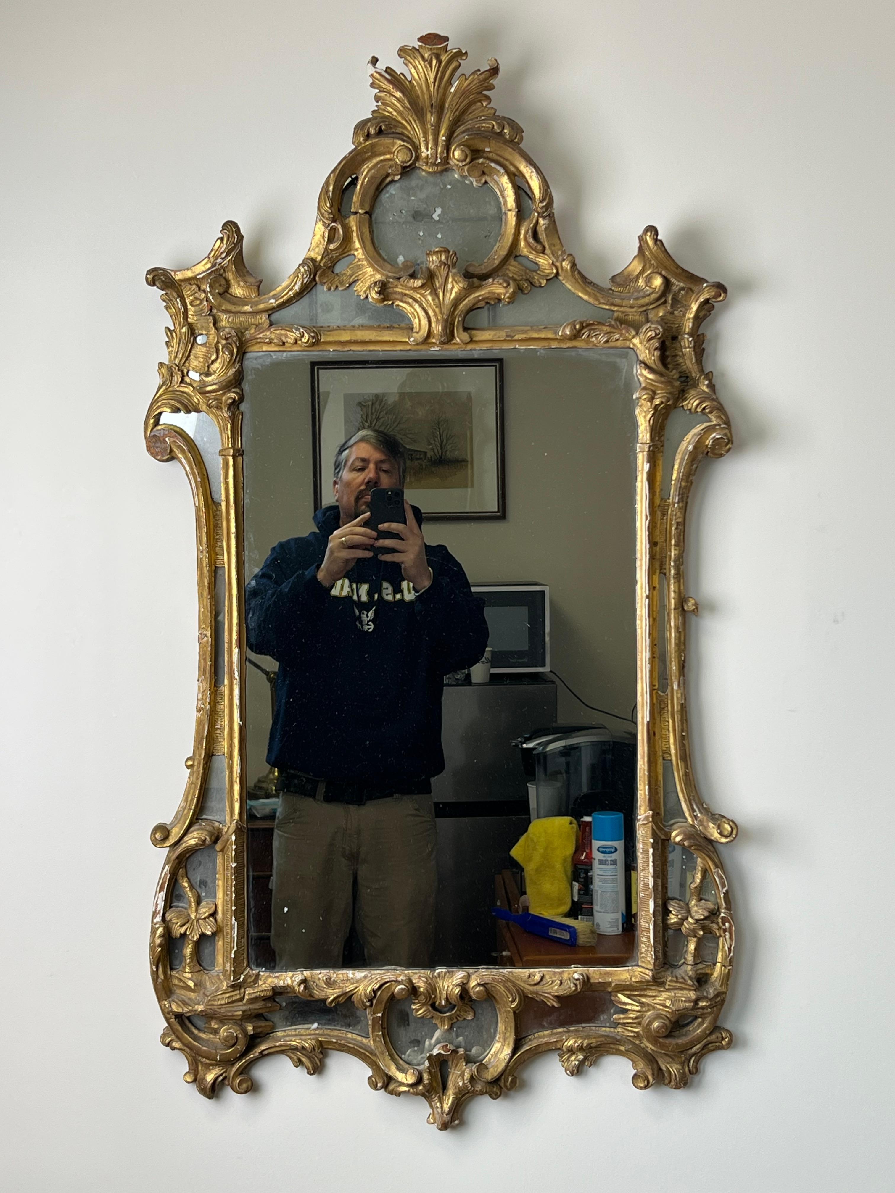 Ce miroir mural antique de la fin du XVIIIe siècle est une magnifique représentation du style baroque orné, avec son cadre en gesso doré et ses étonnants miroirs ajourés. Le cadre, riche en courbes et en détails complexes, est couronné d'une crête