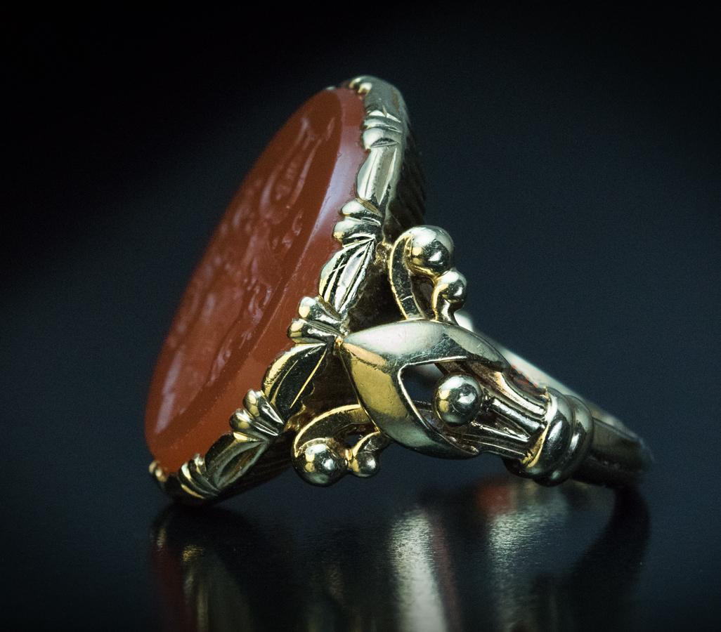 Circa 1880s

This antique 14K yellow gold signet ring from the Victorian era features a carnelian intaglio intricately engraved with a bell-motif coat of arms. The intaglio is set in an ornate bezel flanked by Gothic fleur de lis shoulders.

The