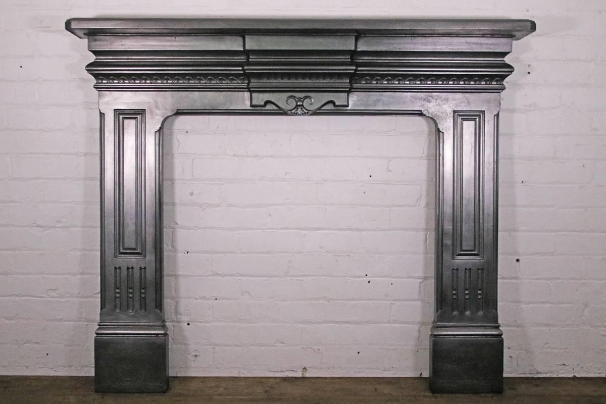 Antique late 19th century Victorian cast iron fireplace surround; the breakfront frieze is decorated with Vitruvian scrolls flanking a fluted center panel, above paneled jambs also benefiting from flutes and reed detail. Dated 1892. 

This