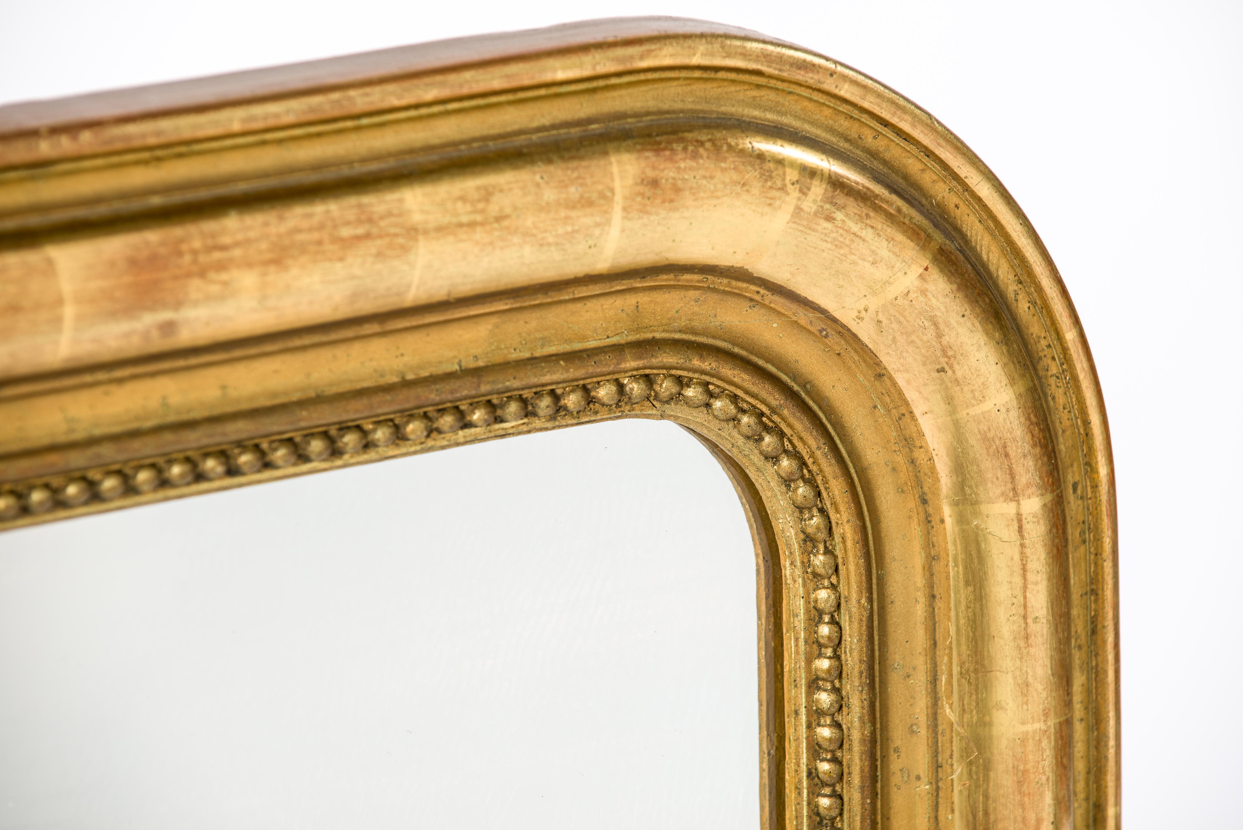 This beautiful antique mirror was made in France in the late 19th century, circa 1890. It features the upper rounded corners typical for the Louis Philippe style. The mirror has a solid pine frame that was smoothened with gesso. A classic pearl