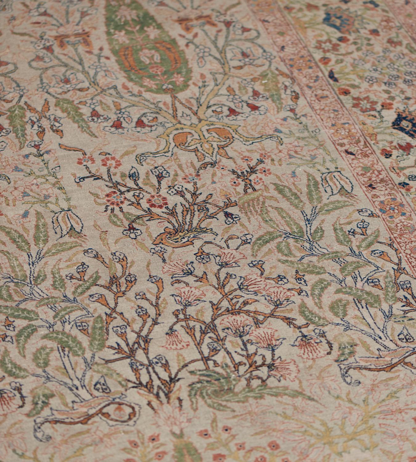This antique Hadji Jallili rug has a central field with rows of shaded green cypress trees surrounded by bands of delicate floral sprays and linked by further floral and leafy vines, in an ivory border of cypress trees alternating with floral and