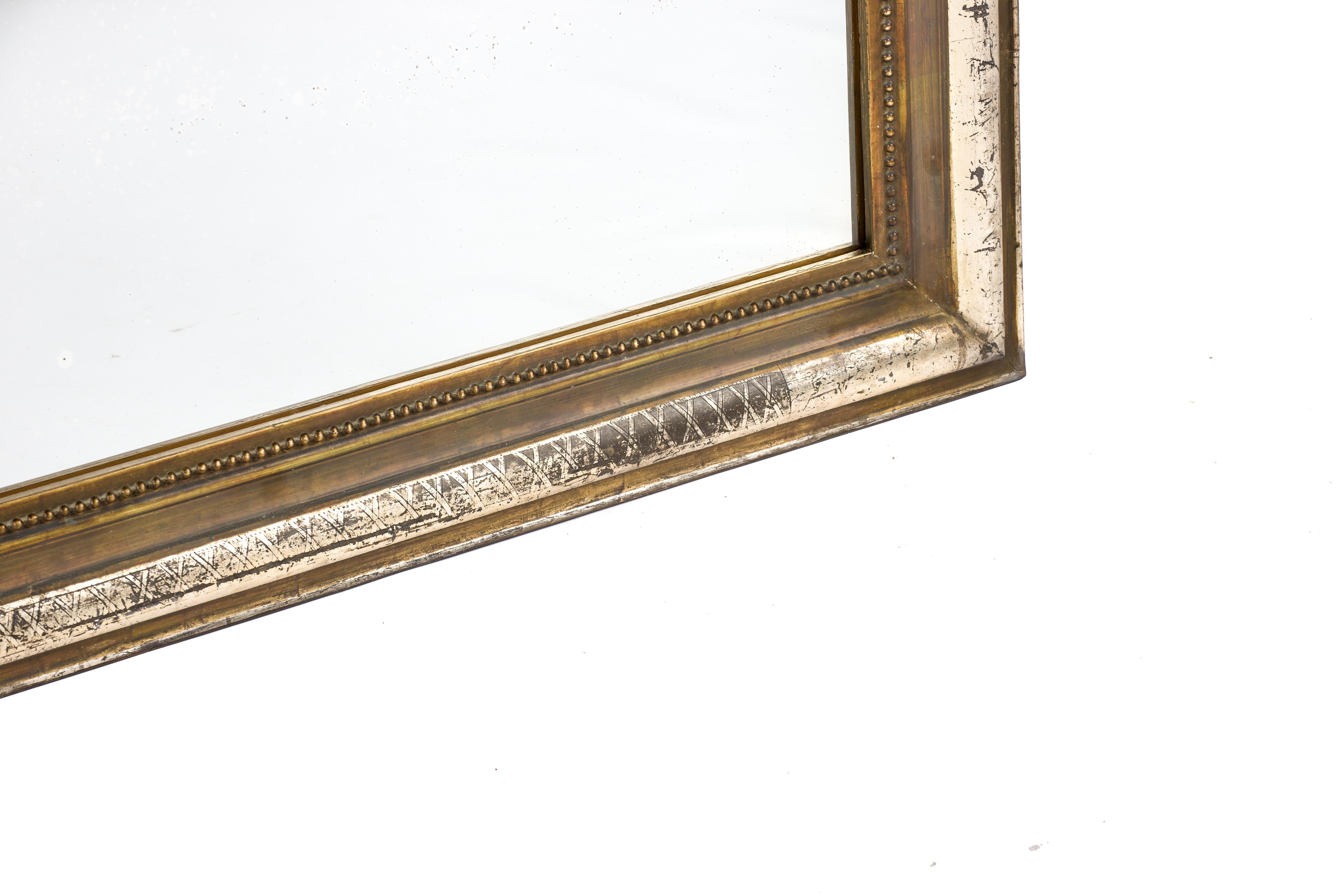 A beautiful and rare antique mirror that was made in northern France in the 1880s. The mirror frame has upper rounded corners typical for the Louis Philippe style. The most elevated part of the frame features a delicate engraved geometric cross