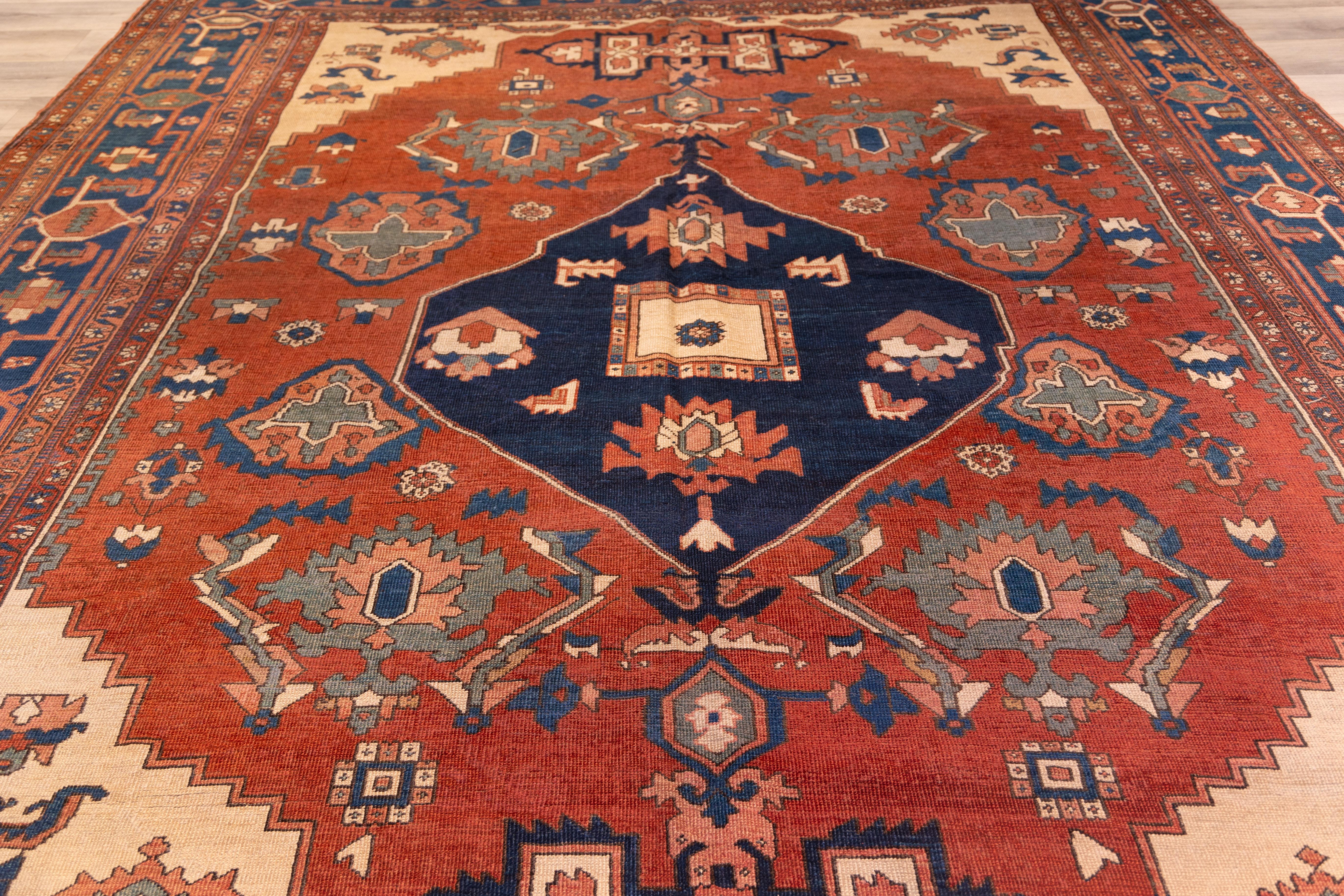 Late 19th century  Serapi featuring a bold primitive central medallion set against a rust red field, framed by crisp ivory corners and a deep navy border. The large-scale Tribal design is rendered in crisp lines with striking contrasts of cobalt,