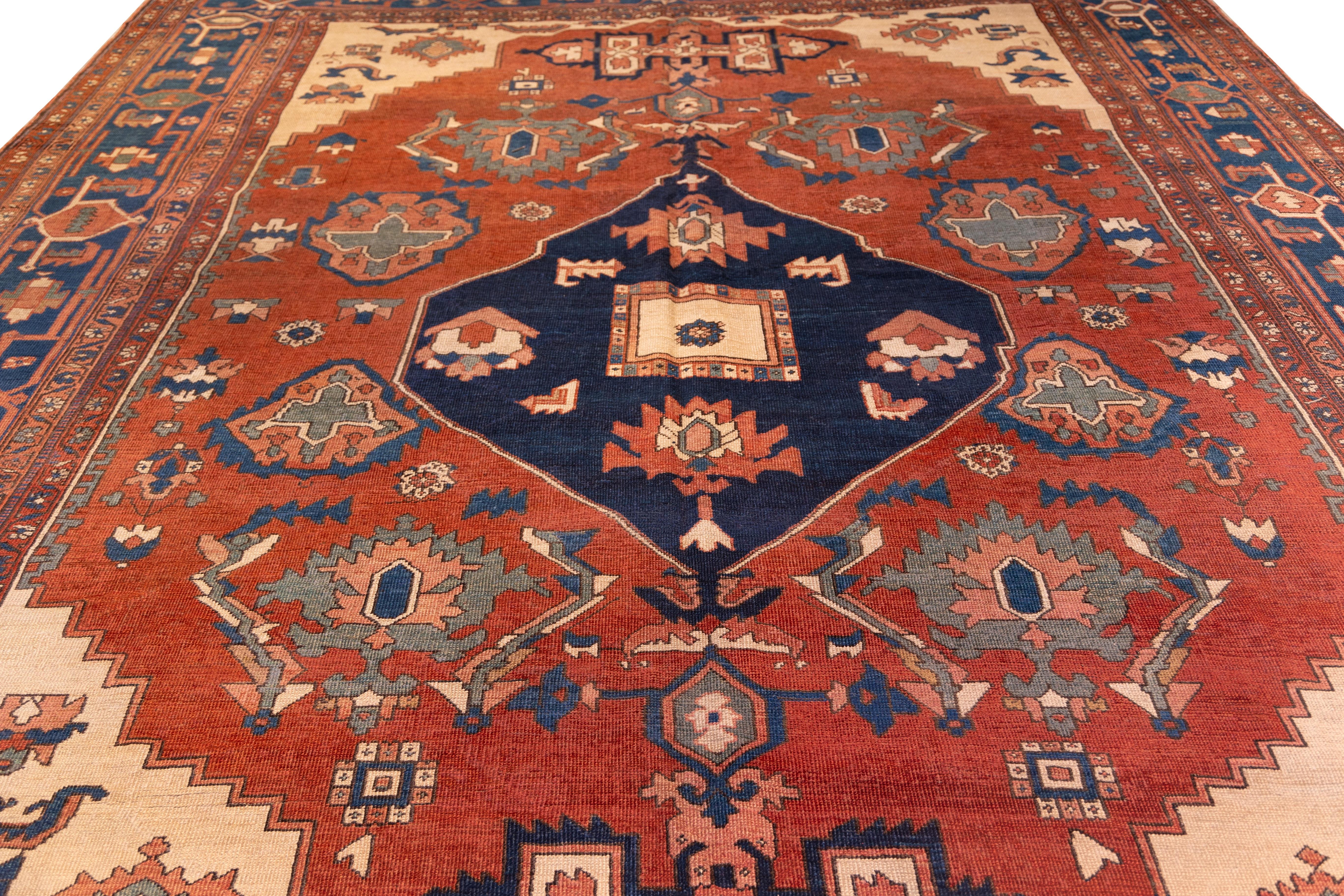 Late 19th century  Serapi featuring a bold primitive central medallion set against a rust red field, framed by crisp ivory corners and a deep navy border. The large-scale Tribal design is rendered in crisp lines with striking contrasts of cobalt,