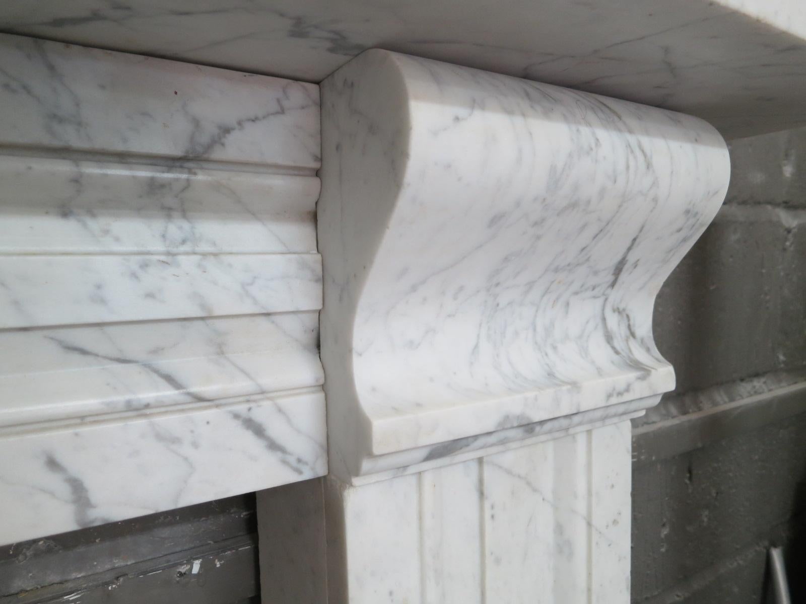 A late Regency period English fireplace of architectural form in pencil vein Italian Carrara marble, with matching moulded jamb and frieze panels. The scrolled corbels with conforming mouldings, supporting a substantial rectangular mantel. The whole