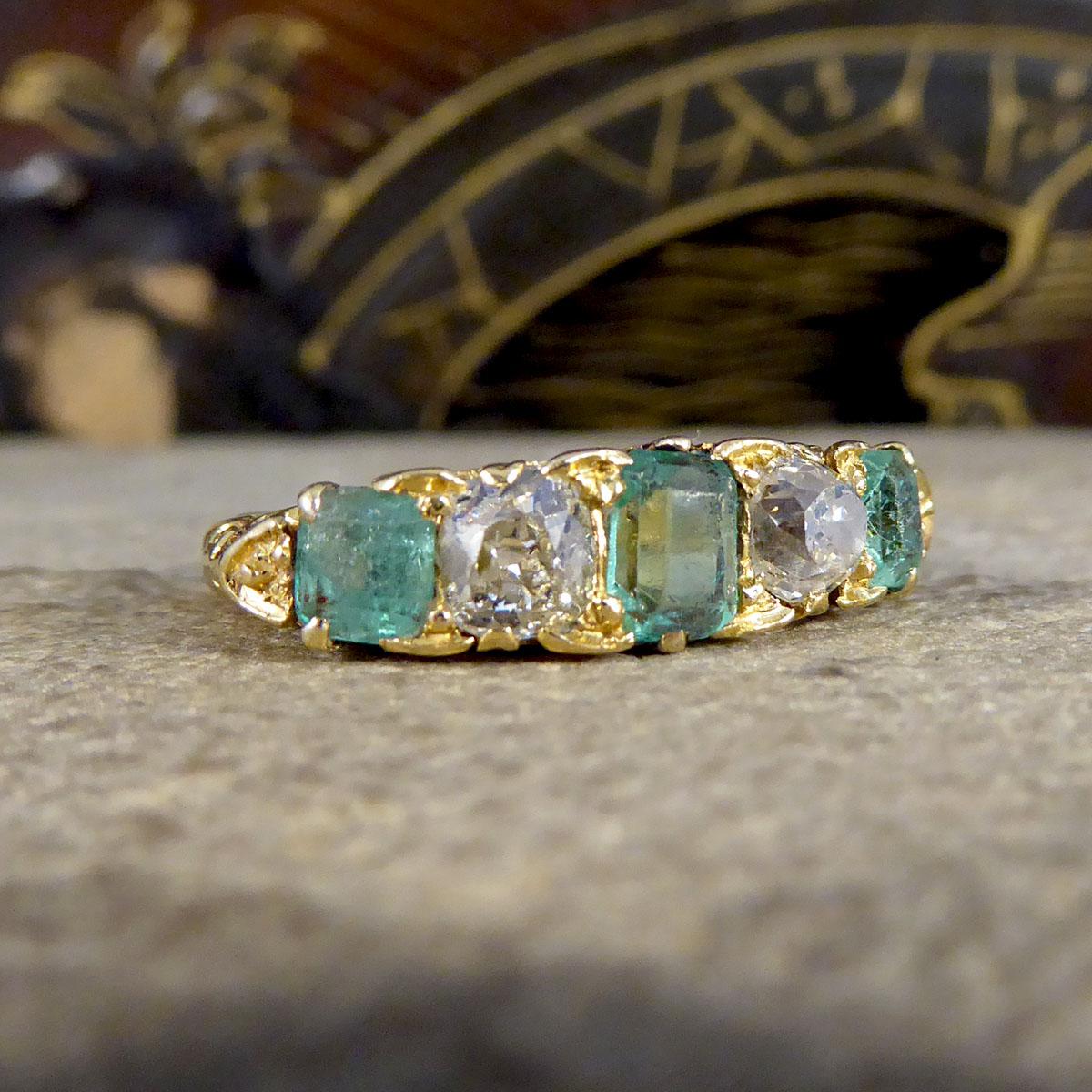 This antique ring was crafted in the late Victorian era. It features a classic swirl gallery and is set in 18ct yellow gold. The emeralds are light and beautiful in colour with an even colour distribution, and have wear and tear that is consistent