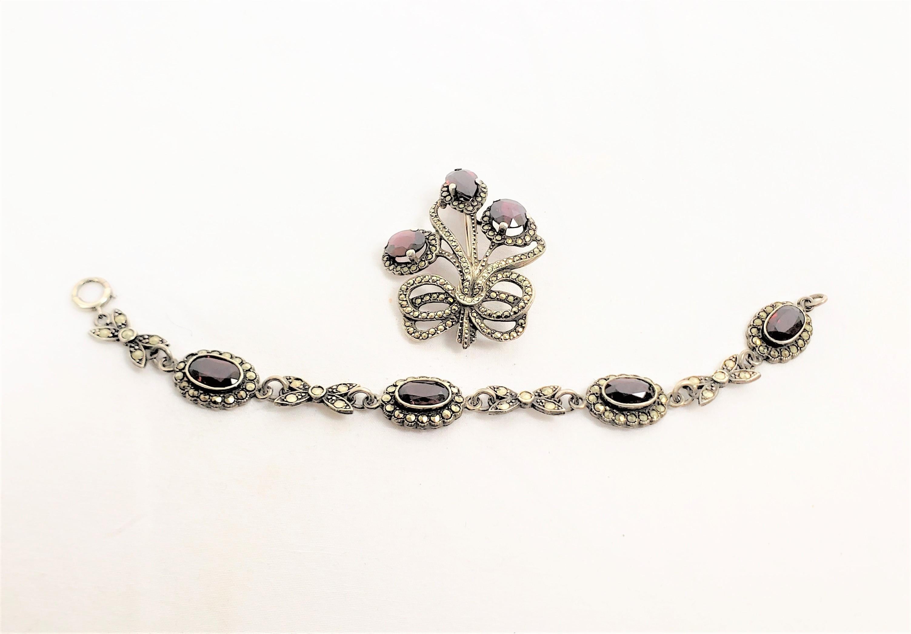 This antique brooch and bracelet set is signed by an unknown maker, and originated from England and dates to approximately 1900 and done in the period Late Victorian style. The set is composed of sterling silver with prong set cut garnet stones in