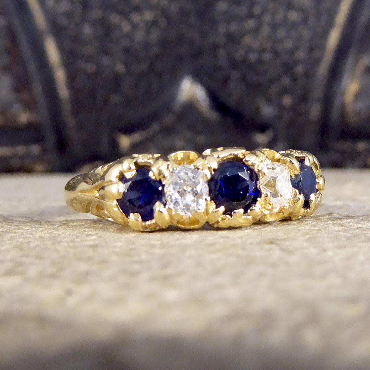 This lovely antique ring was created in the Late Victorian era with a beautifully detailed 18ct Yellow Gold gallery and carved shoulders. It holds three sparkling deep blue Sapphires weighing approximately 0.62ct in total and two smaller Old