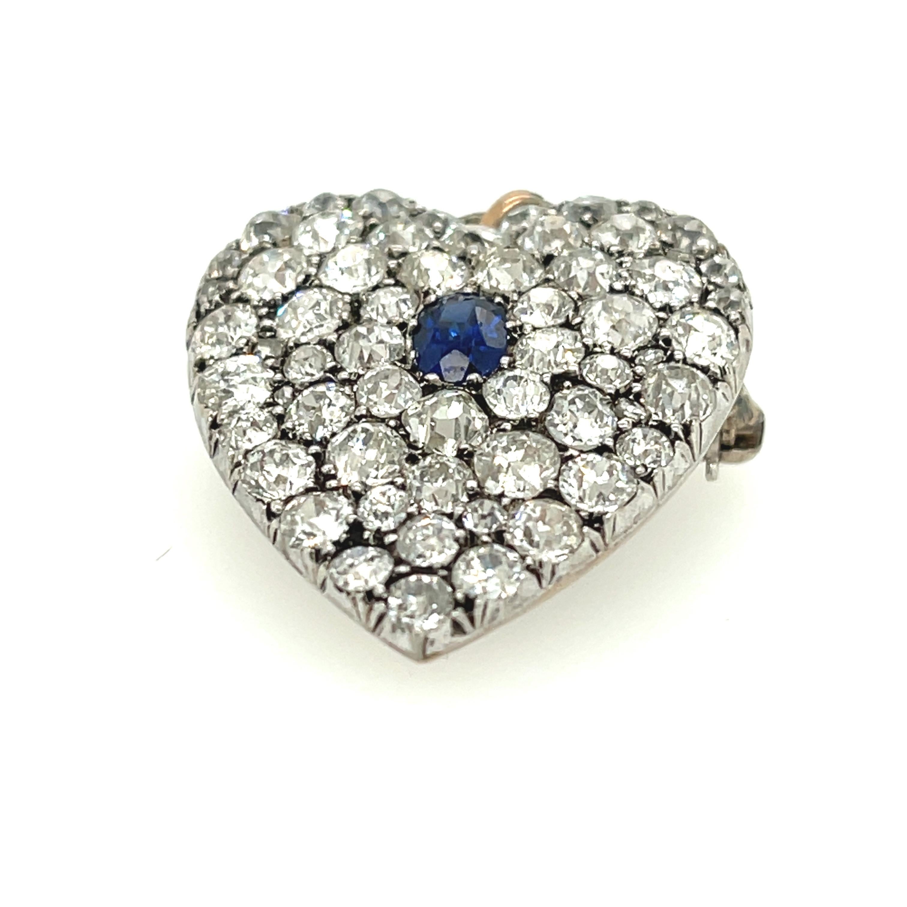 A antique late Victorian pave diamond heart pin pendant set with an oval sapphire circa 1890. The pin is made in silver and gold, and is set with old mine cut and rosecut diamonds. There are 61 diamonds weighing approximately 5.00 carats. There is a