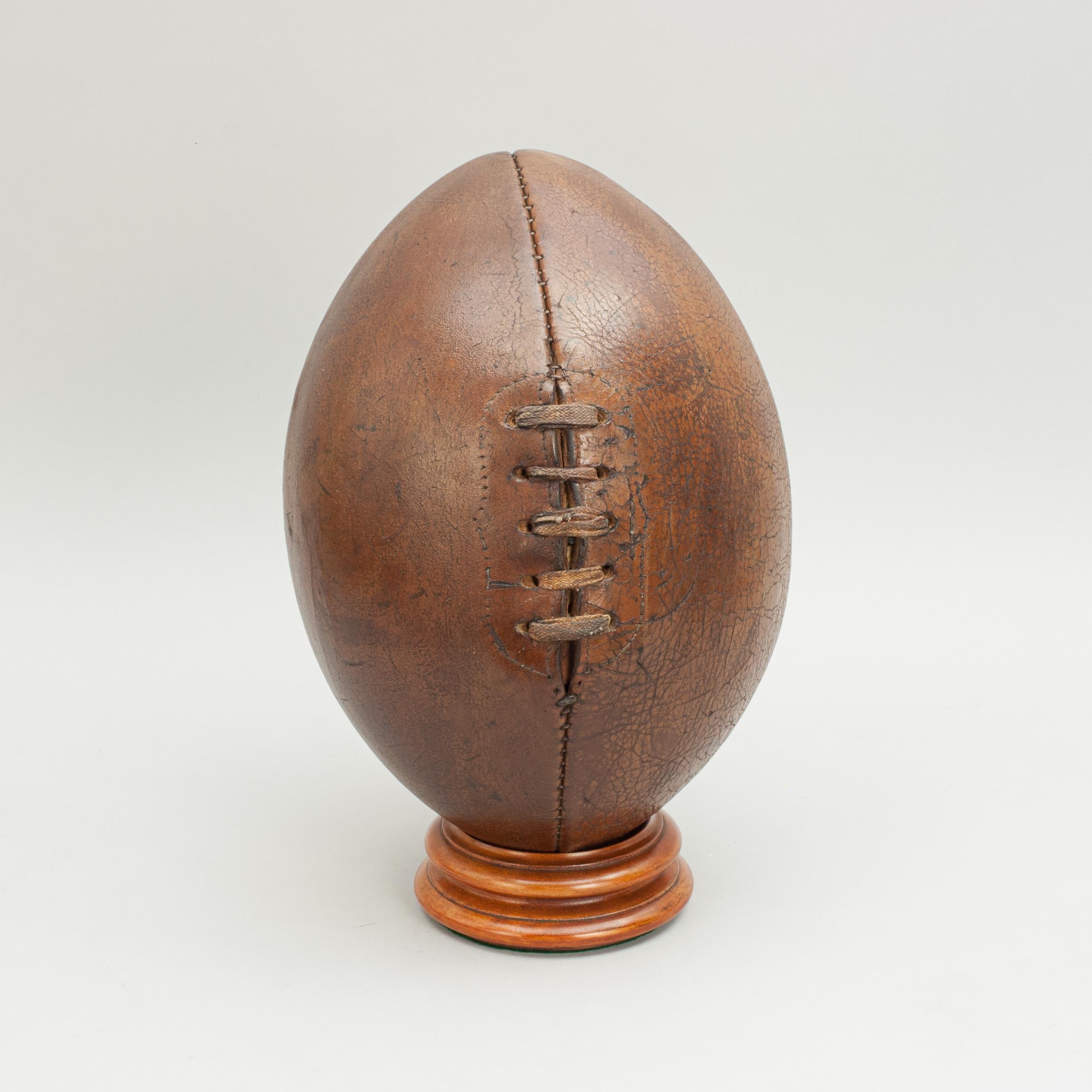 Vintage leather rugby ball.
A traditional four panel leather rugby ball with a lace-up slit to the top and valve for bladder inflation. The ball is with good dark brown colour and patination. The ends of the ball are semi-round.

Stand sold
