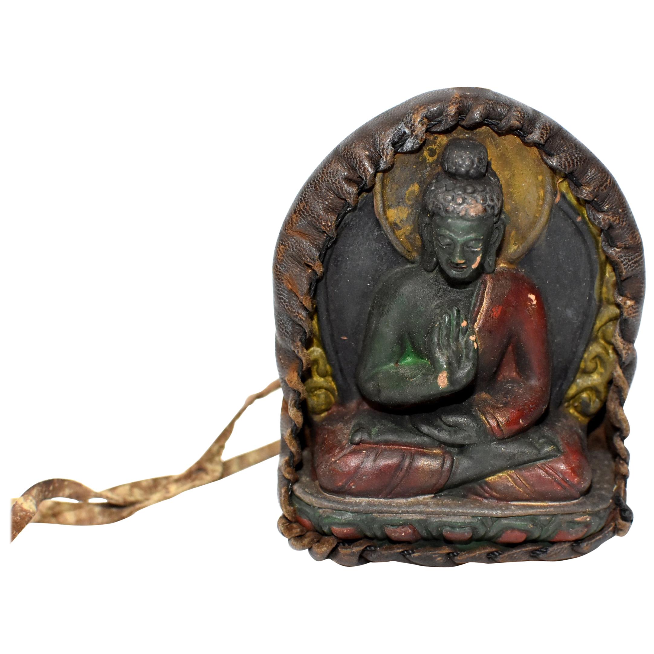 A Tibetan amulet featuring Buddha encased in a handmade leather shrine. Buddha is made of terracotta, beautifully crafted displaying well defined facial features, decorated robe and a wonderful smile. Featured is Buddha in abhaya mudra, a protection