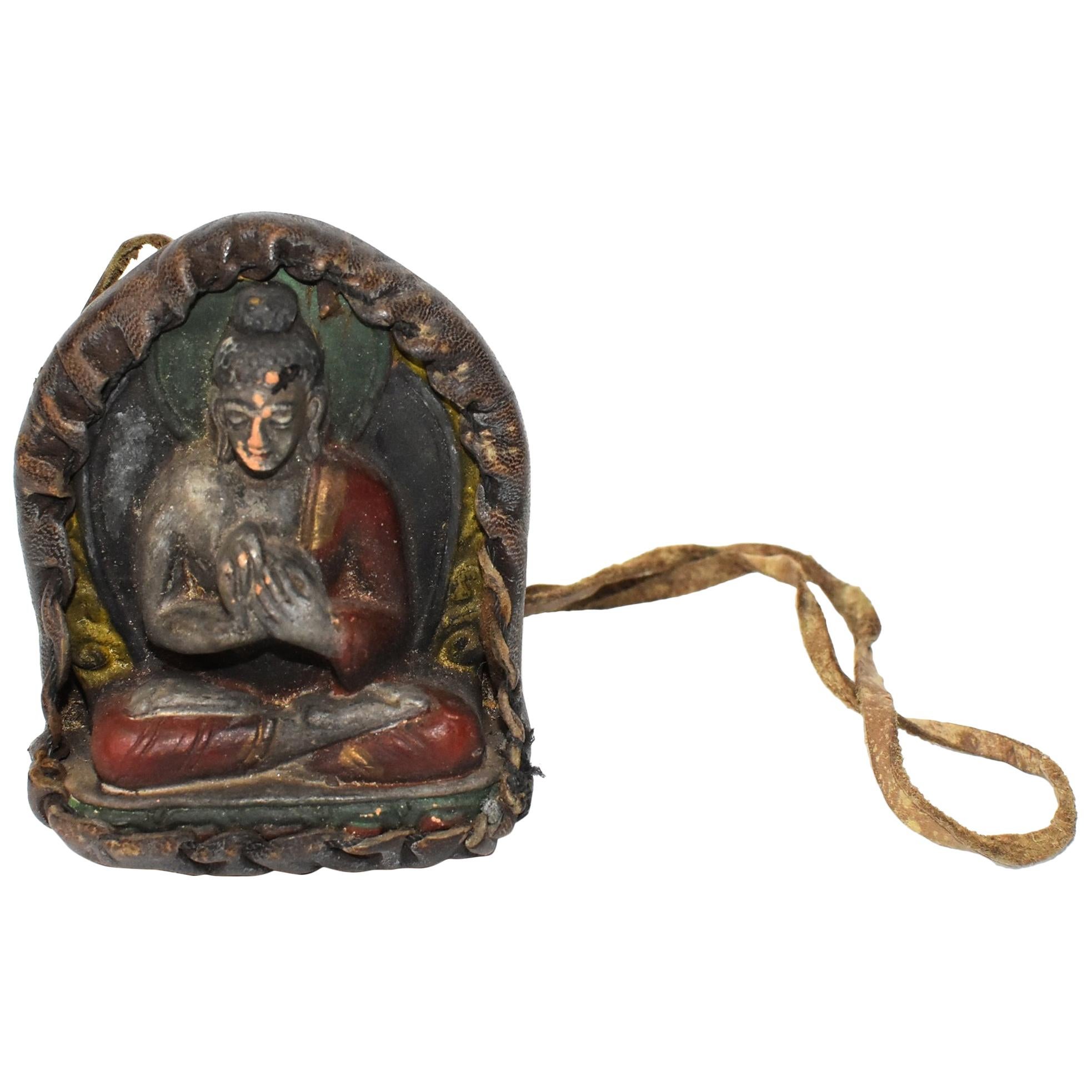 A Tibetan amulet featuring Buddha encased in a handmade leather shrine. Buddha is made of terracotta, beautifully crafted displaying well defined facial features, decorated robe and a wonderful smile. Featured is Buddha in dharmachakra mudra, a