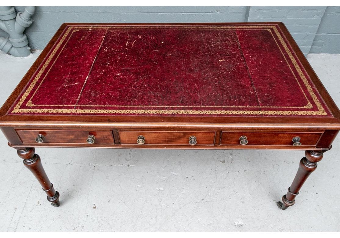 A wide mahogany desk with carved top edge and inset gilt tooled oxblood leather top. Each side with three figured mahogany apron drawers with brass knob pulls with rosette centers and dove-tail construction. Raised on fine turned legs on casters.