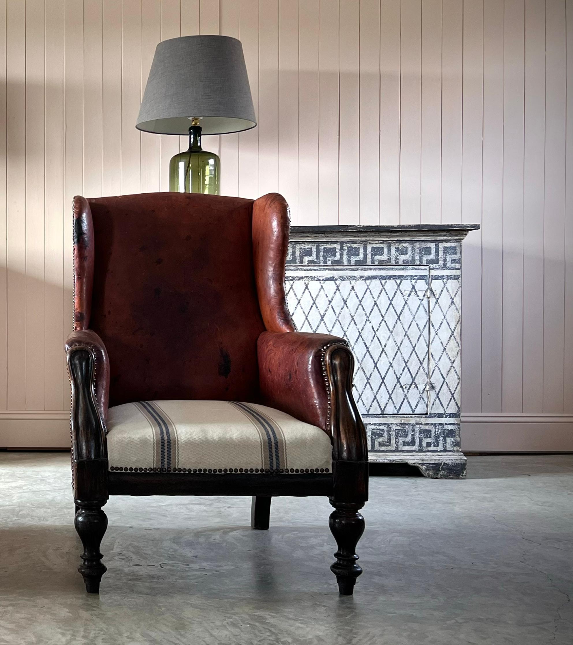 Dieser Lederstuhl aus der Mitte des 19. Jahrhunderts hat eine fantastische Farbe und Patina.  Jede Menge Charakter und Textur. Der Ohrensessel wurde ursprünglich entworfen, um Zugluft abzuhalten und die Wärme des Feuers drinnen zu halten - heute ist