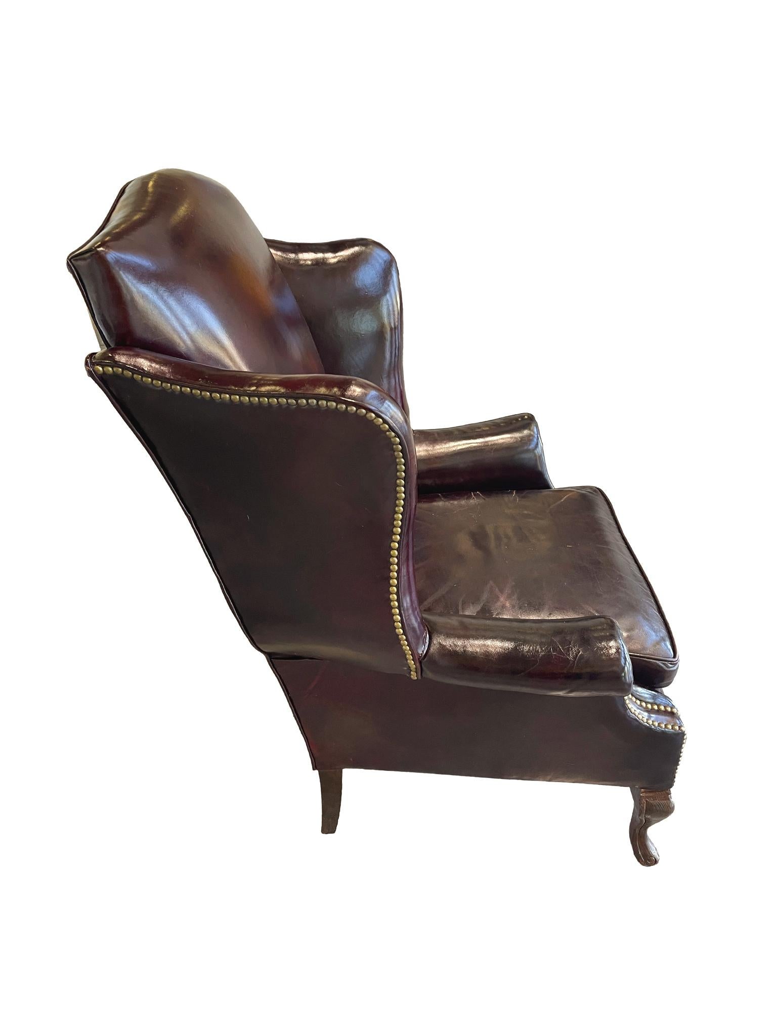 Early 20th century Queen Anne-style wingback, with beautifully aged burgundy-toned leather, brass stud trimming, and cabriole front legs.

Dimensions:
28 in. depth
33 in. width
22 in. interior width
47 in. height
20.5 in. seat height

Condition