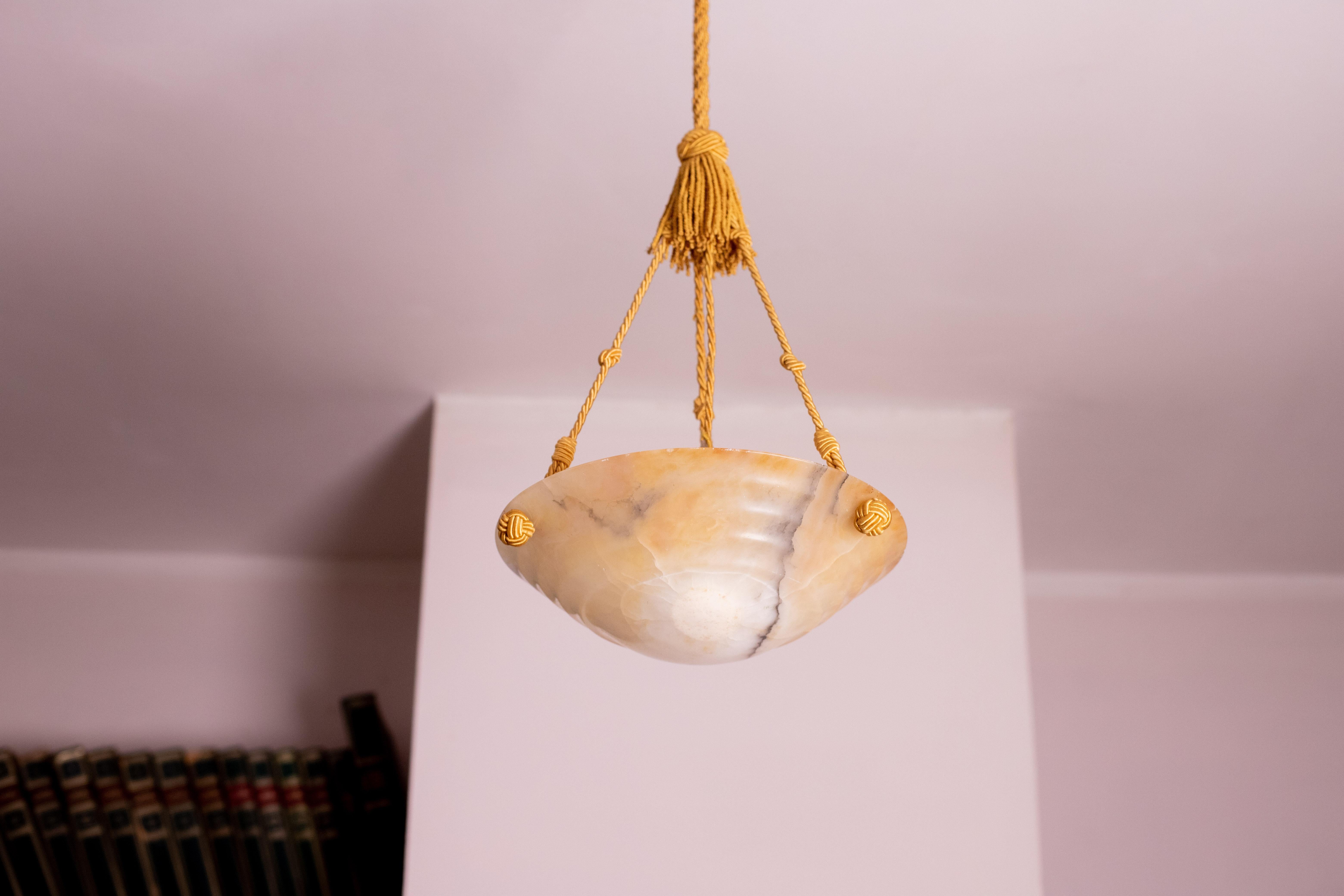 Antique alabaster hanging chandelier in Art Deco style, circa 1940s.
A unique alabaster piece, beautifully crafted with shades and reflections of other colors when lit, suspended by three strings (wires).
The light that shines through the