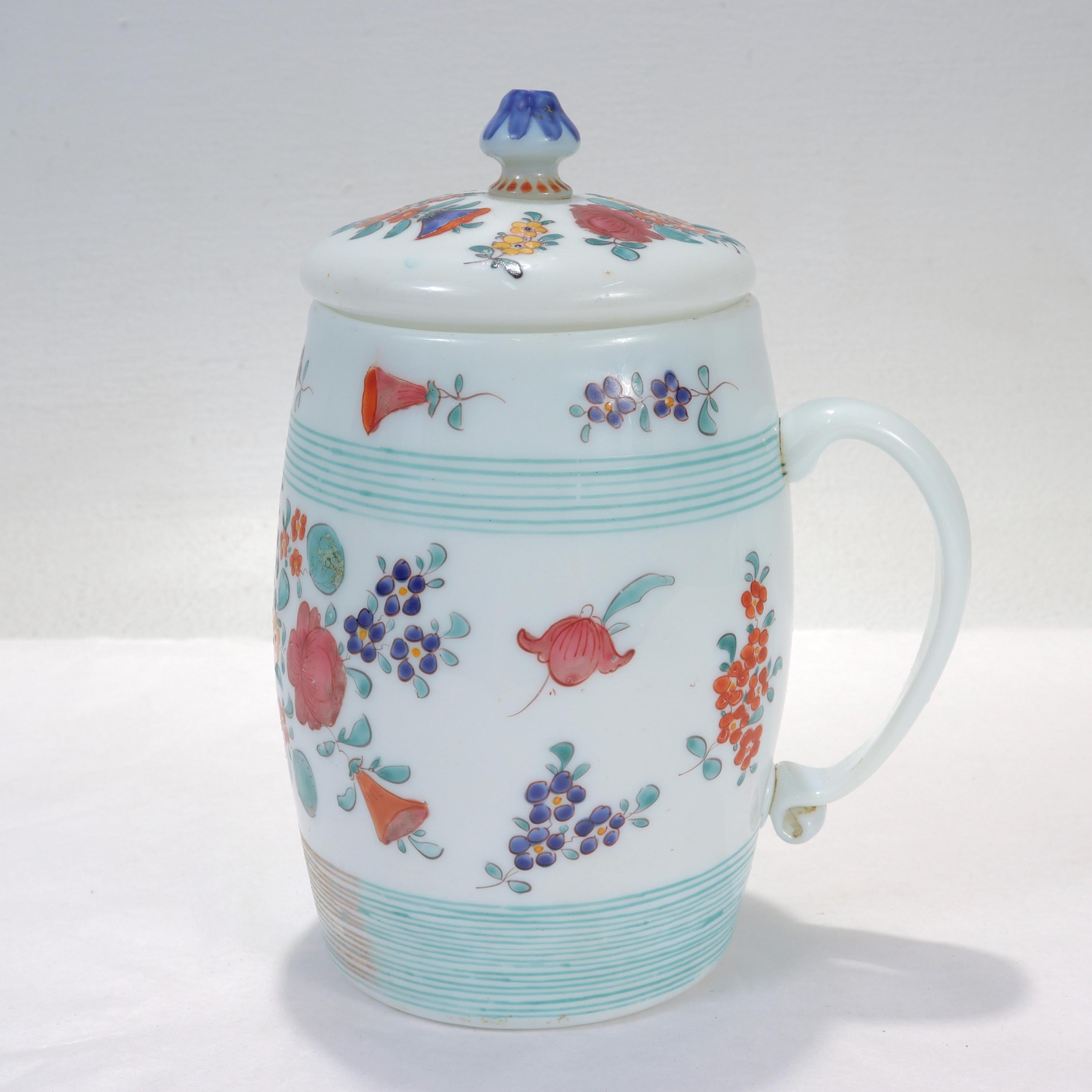 A fine antique glass beer stein.

Consisting of a handled stein with a lid decorated throughout with hand painted enamel floral motifs and green lines.

The lid has a finial decorated with blue & red accents. 

Simply a wonderful early Milchglas