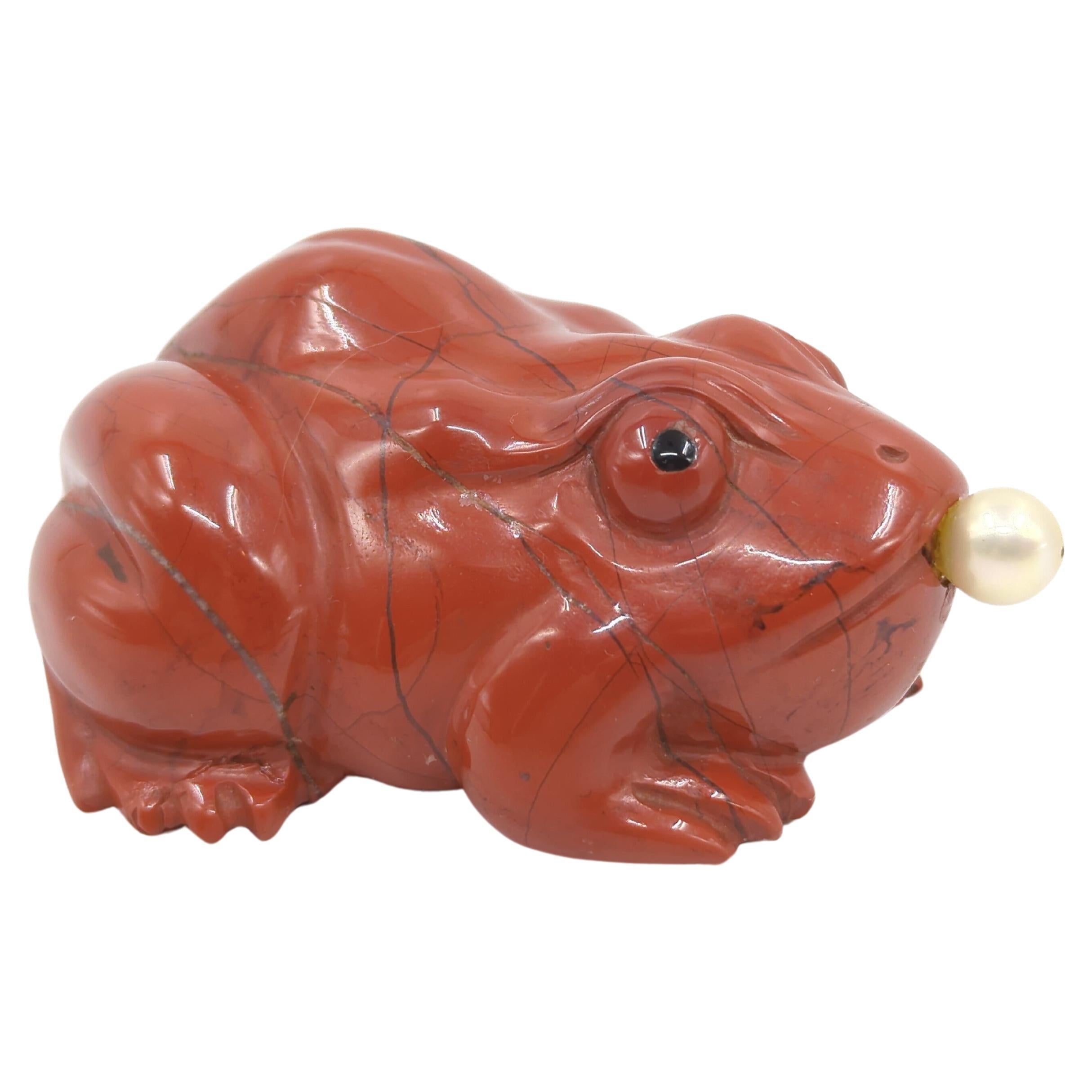 A large antique Chinese hand carved red jasper snuff bottle, in the form of a sitting frog, life like in size and details, eyes painted black, with a pearl stopper to its mouth attached to a pointy metal spoon

circa: 1900-1930
Weight: 196 grams