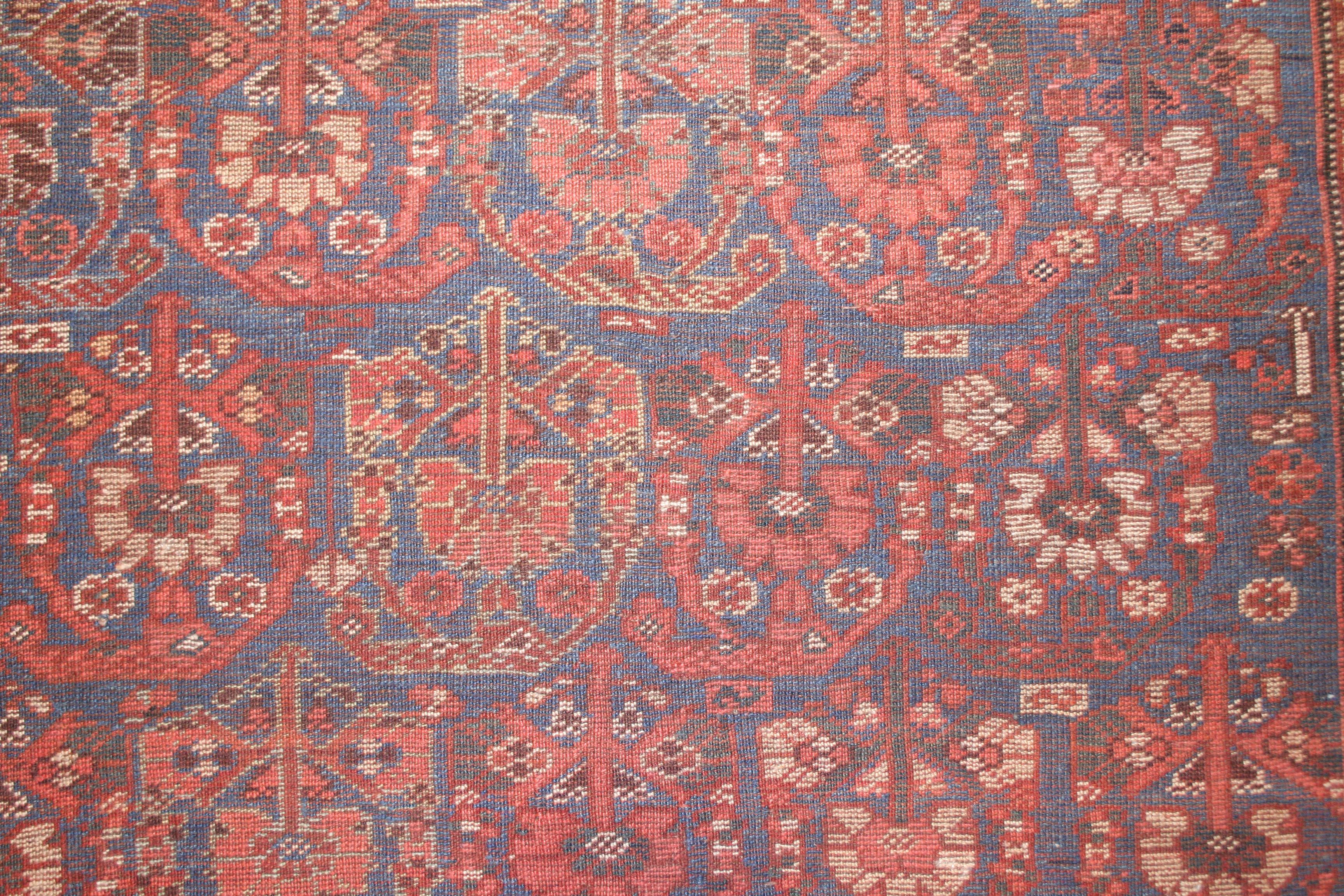 Tapis finement noué de la tribu Khamseh, située près de Shiraz, se distinguant par un fond indigo clair embelli par des rangées parallèles et décalées de paisleys stylisés. Ce motif a été adopté ici à la fois pour le champ et pour la bordure, la