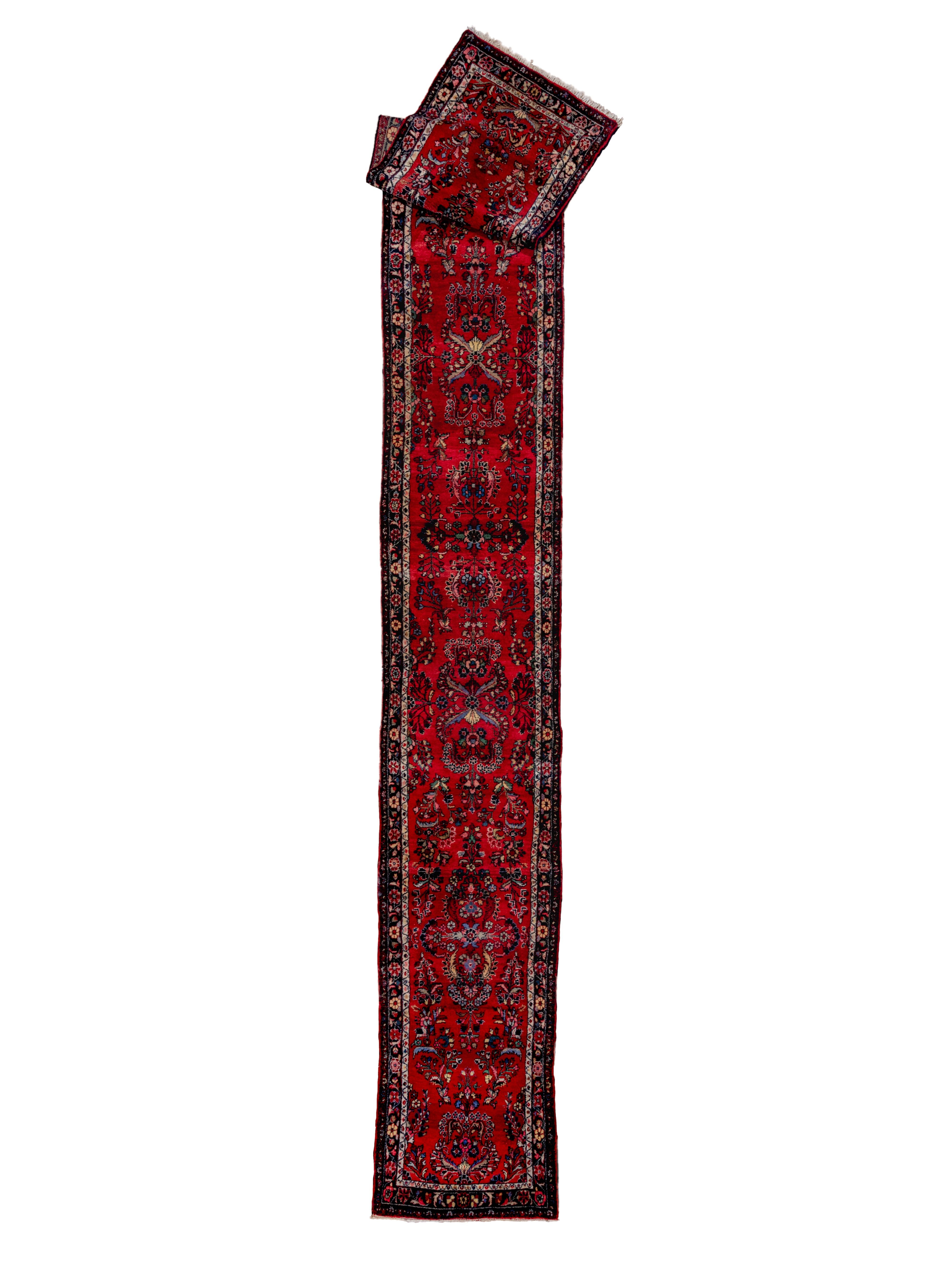 In the “American Sarouk” design of detached floral sprays on a red ground, this kenare (runner) was destined for the American market.  It is accented with a selection of blue tones along with ivory and straw. The navy blue border shows leaf-winged