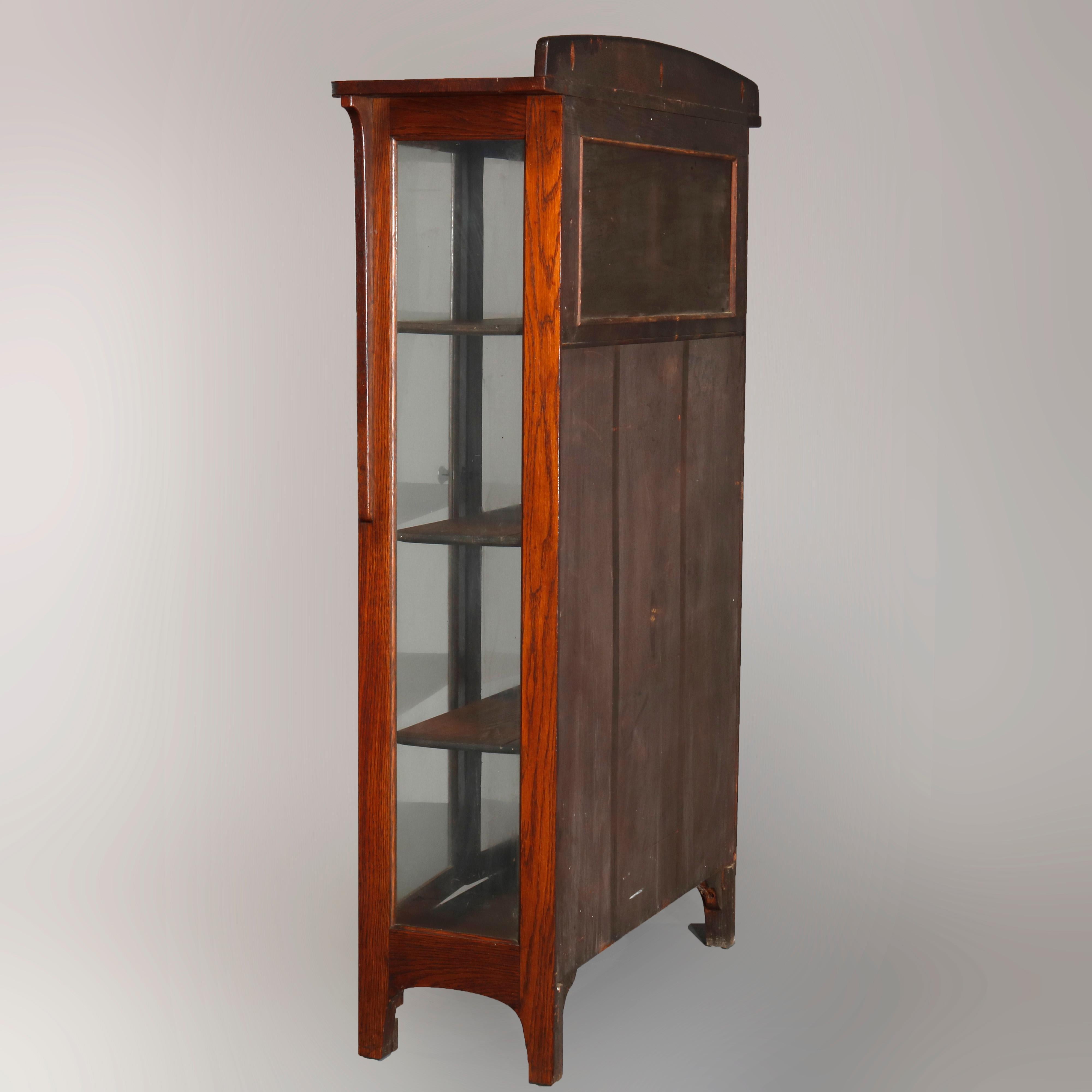 An antique Arts & Crafts mission oak china cabinet attributed to Limbert offers oak construction with arched backsplash surmounting case with double glass doors opening to shelved interior, raised on straight legs with arched corbels, circa