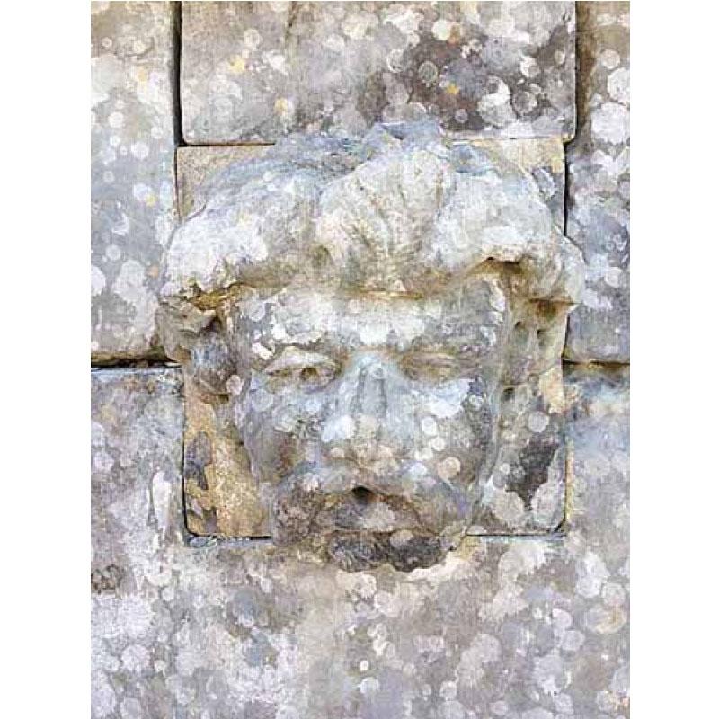 Here we offer a unique limestone wall fountain that honors the Roman god of wine Bacchus. This piece boasts a basin carved from a single boulder complete with a wall cap and an over sized crown carved from a single stone. The patina on the stones
