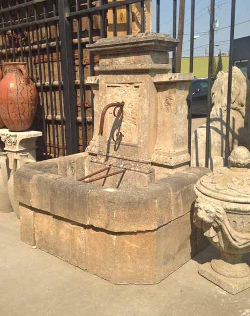 Here we offer an antique limestone wall fountain with an iron spout. This piece has very sharp carvings on the crown and back plate with carved panels married to either side. The basin wall is rounded off at the top and has a slight overhang in the