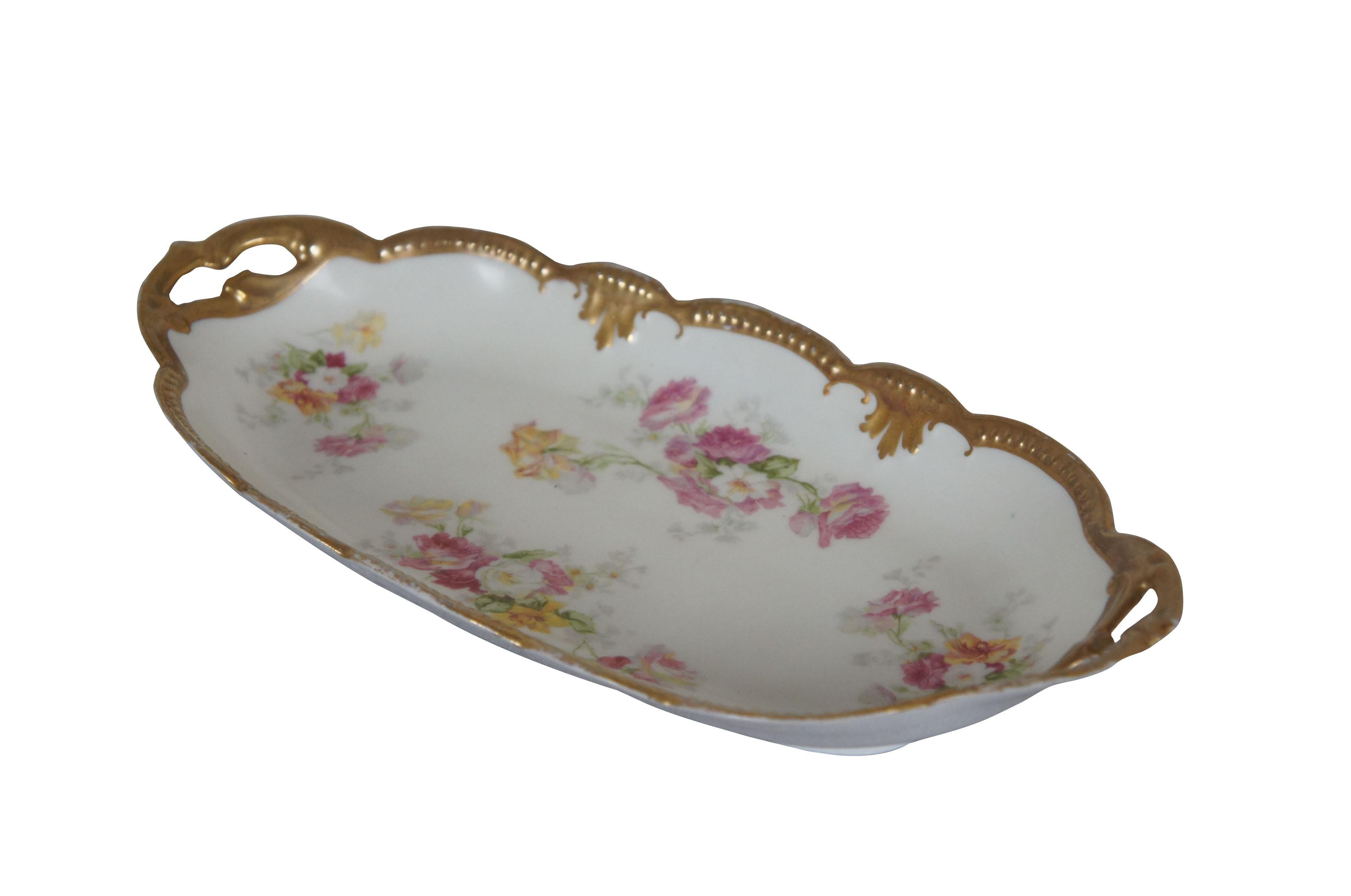 Early 20th century Limoges porcelain serving dish / vanity tray by Alfred Klingenberg and Charles Dwenger. Long oval shape with scalloped edges and pierced handles. Gilded border. Sprays of pink, yellow, and green flowers. Mark used circa