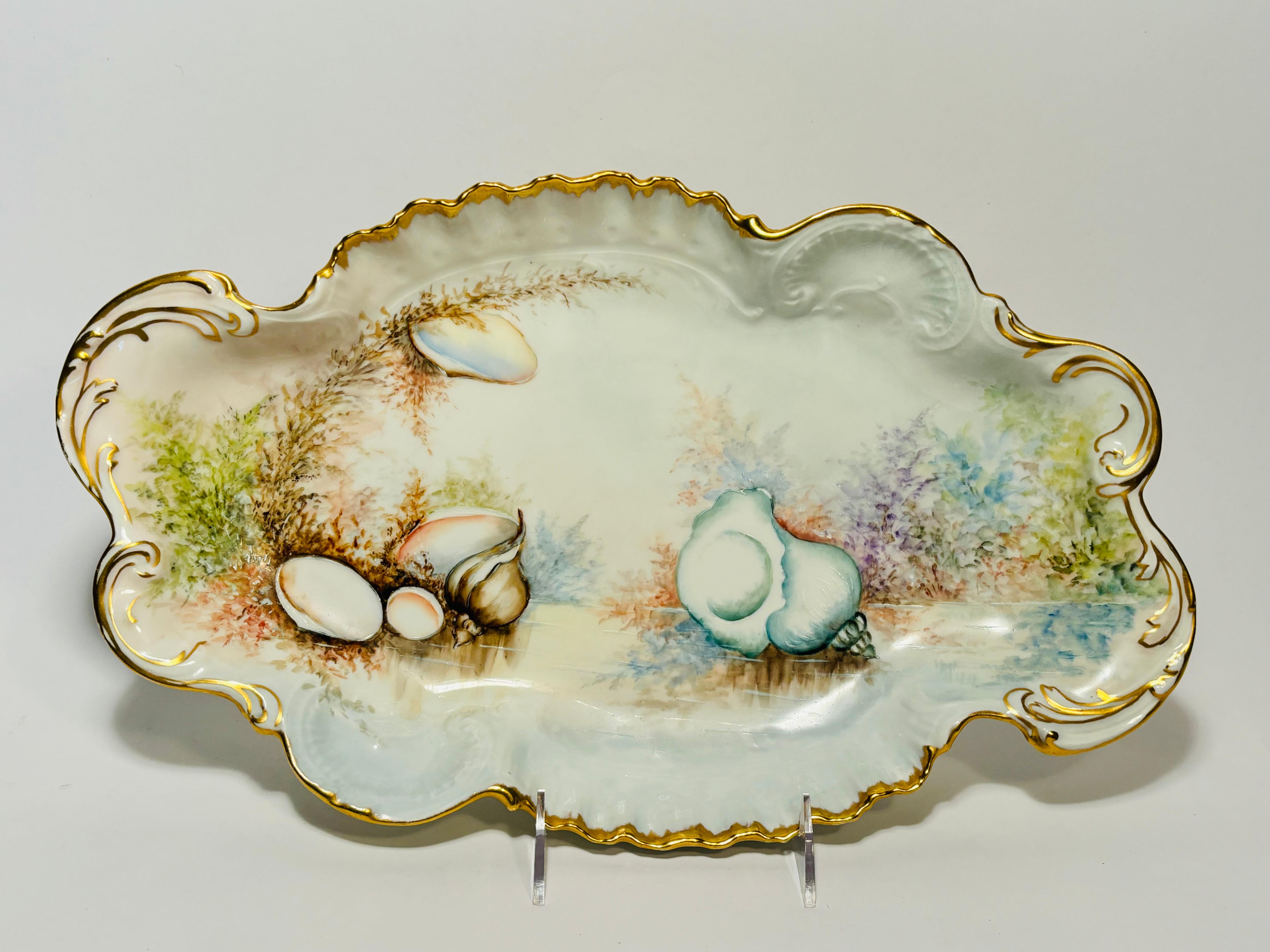 A lovely centerpiece for your display and a nice sized serving platter featuring a scalloped shape with impressed shell cartouches in the porcelain blank. Trimmed in 24 karat gold and nicely hand painted all over with realistic shells and vibrant