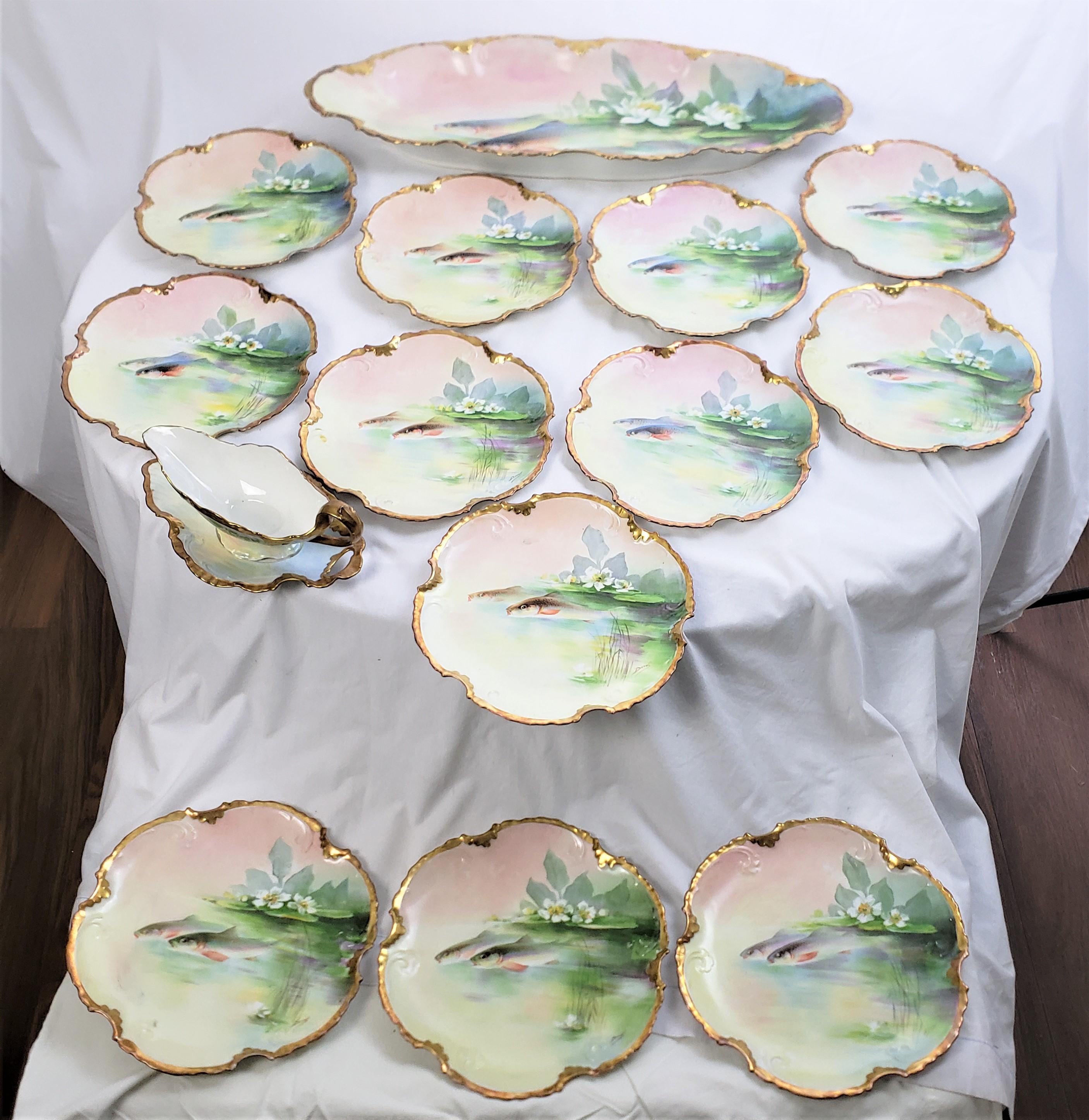 This antique fish serving set was made by the renowned Limoges factory of France in approximately 1880 in the period Late Victorian style. The set is composed of porcelain and consists of twelve scalloped plates, an extremely large serving platter