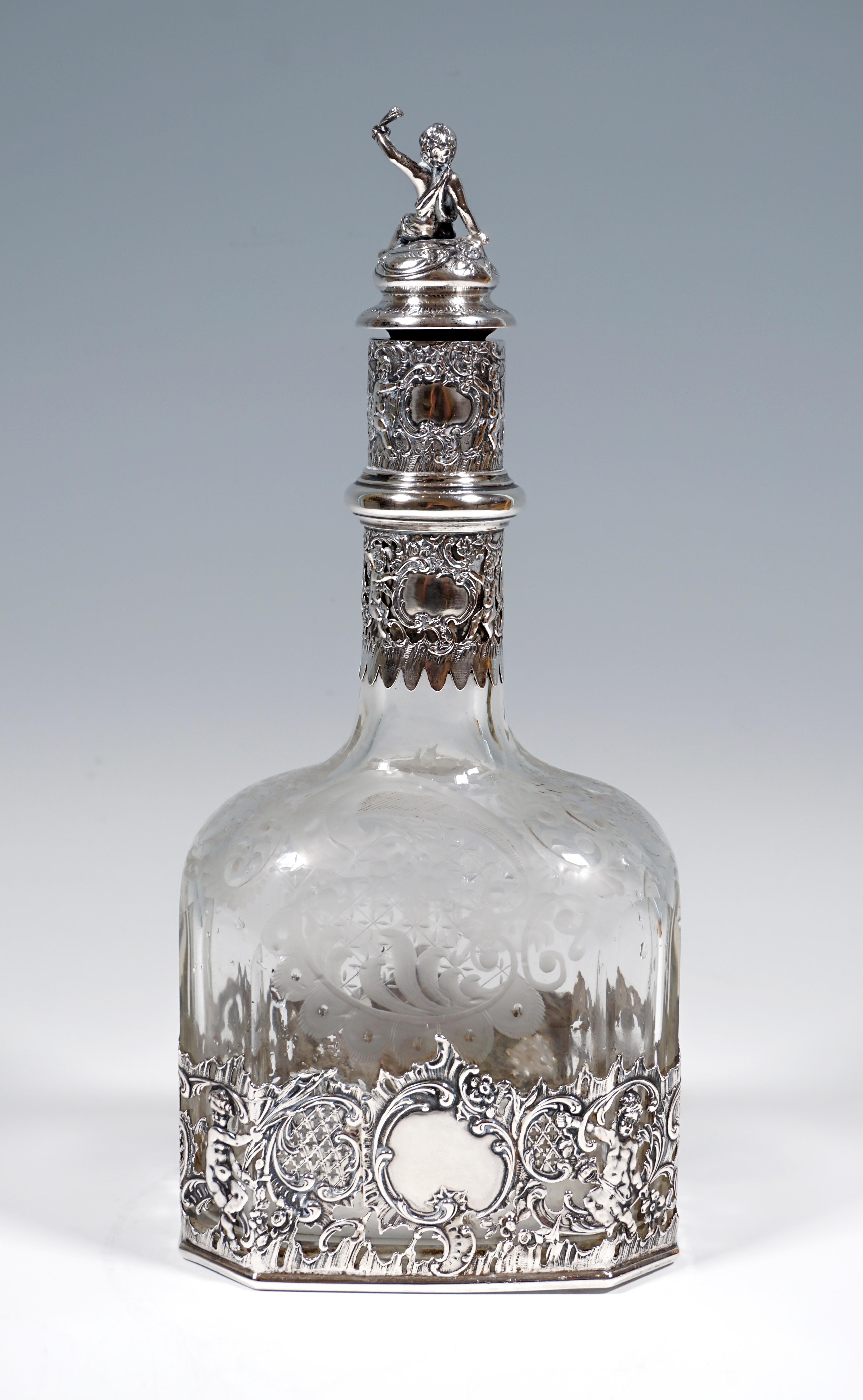 Elaborately crafted liqueur bottle made of clear glass on a rectangular floor plan with bevelled corners, in the stand area and on the slender neck framed by openwork silver fittings with cartouches, rocailles and putti, 
cork closure piece with