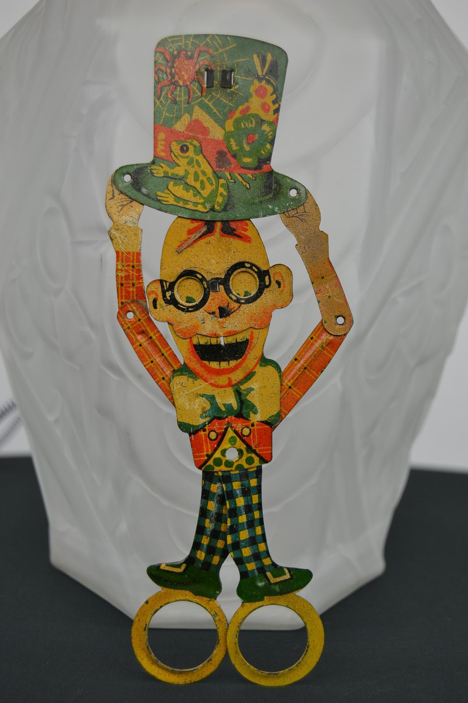 1920s cute looking lithographic tin scissor toy by Distler Germany. 
This charming Antique Mechanical Toy 
shows Harold Lloyd, known as a silent movie comic star. 
When you close the scissor, the hands pull the hat up an the glasses are also