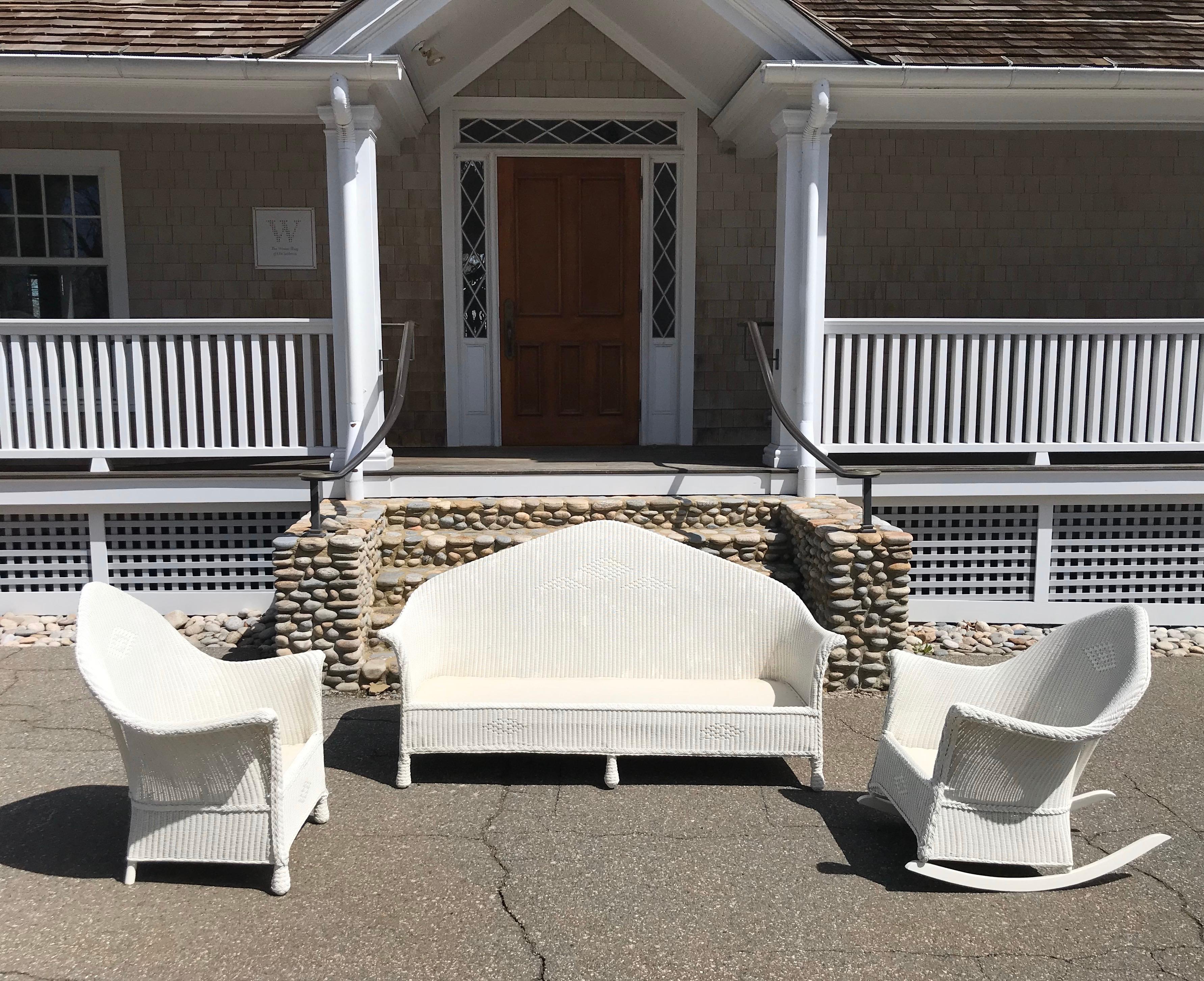 Three-piece antique wicker Lloyd Loom set in fresh white paint. White fabric covers spring seat platform. Sofa measures 70” wide, 36” tall, 31” deep with seat platform of 13”. Chair measures 35” tall, 30” wide, 26” deep with seat platform if 13”.