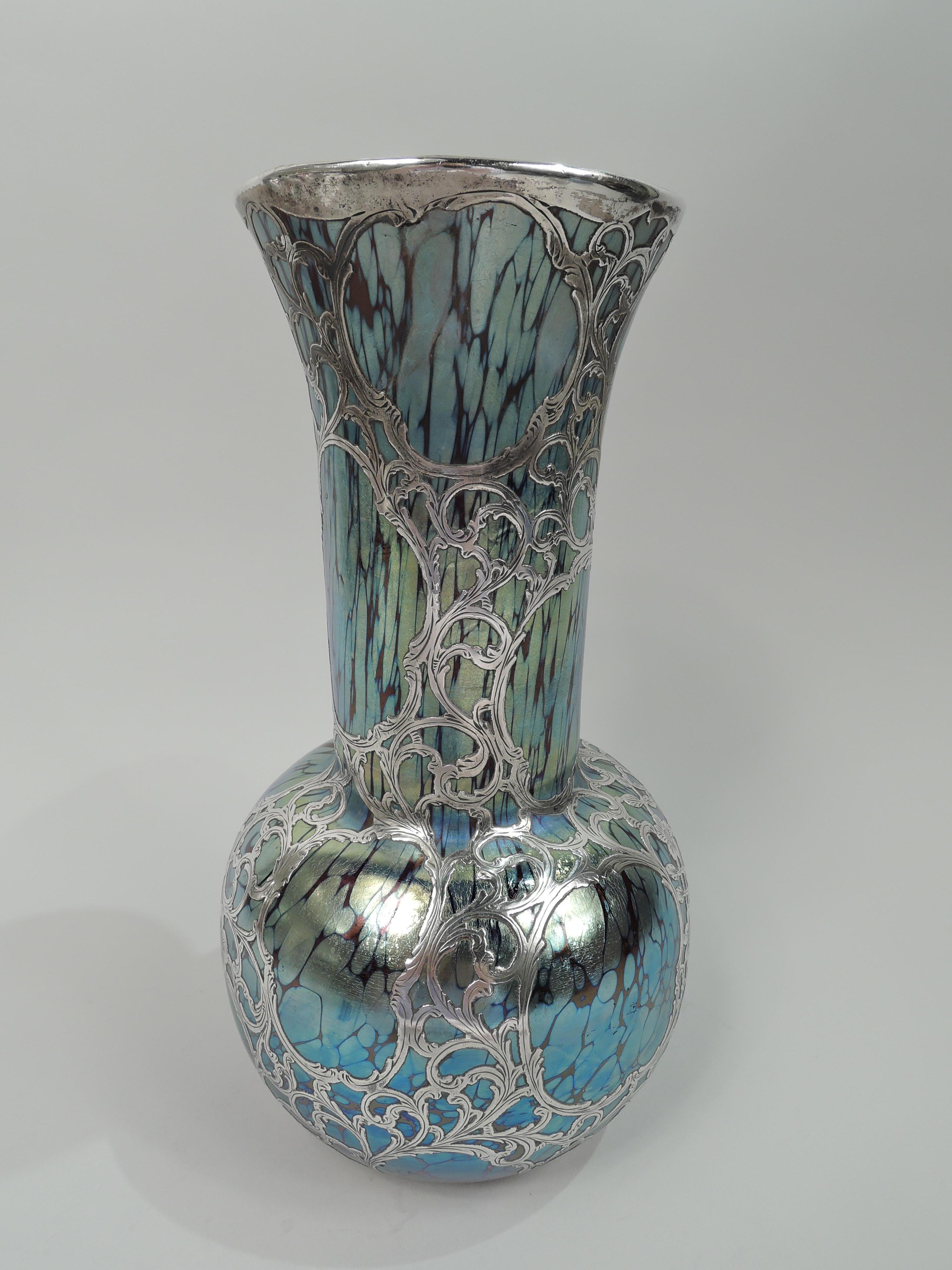 Turn-of-the-century Art Nouveau glass vase by historic Loetz with engraved silver overlay. Globular with tall cylindrical neck and gently flared rim. Overlay in form of dense leafing and flowering scroll pattern with open scrolled cartouches. Solid