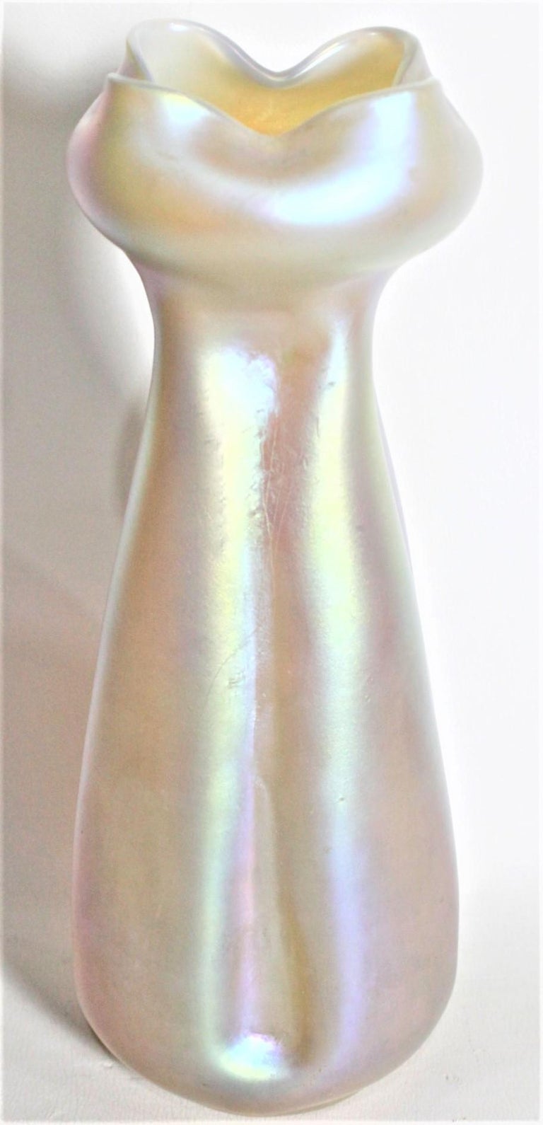 This antique art glass vase is unsigned but was made by Loetz of Austria in circa 1920 in their period Art Deco style. This pale yellow iridescent or 'Candis Silberiris' art glass vase has indented sides and a bulbous crimped top. This vase stand