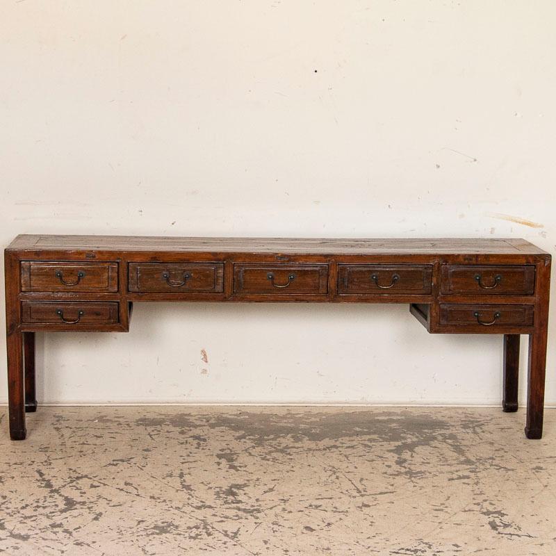 Long and narrow, this handsome elm console table has clean straight lines balanced with 7 drawers creating a functional and appealing aesthetic fit for any modern home. Crafted in the late 1800s, notice the expected age-related scratches, wear and