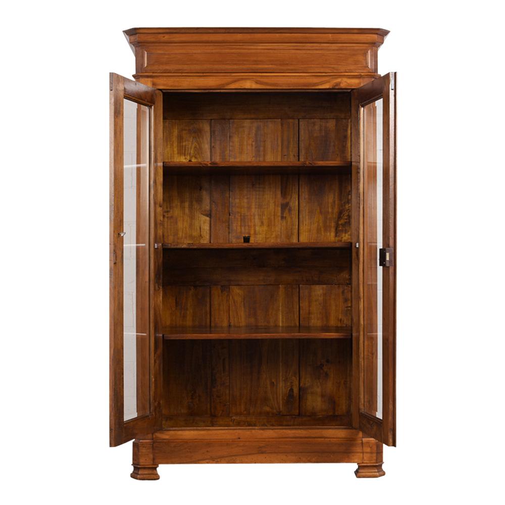 This French 19th century Louis Philippe bookcase has been restored and is made from walnut wood with the original walnut finish. The top of the bookcase has a large carved crown molding. It comes with two tall beveled glass doors with carved molding
