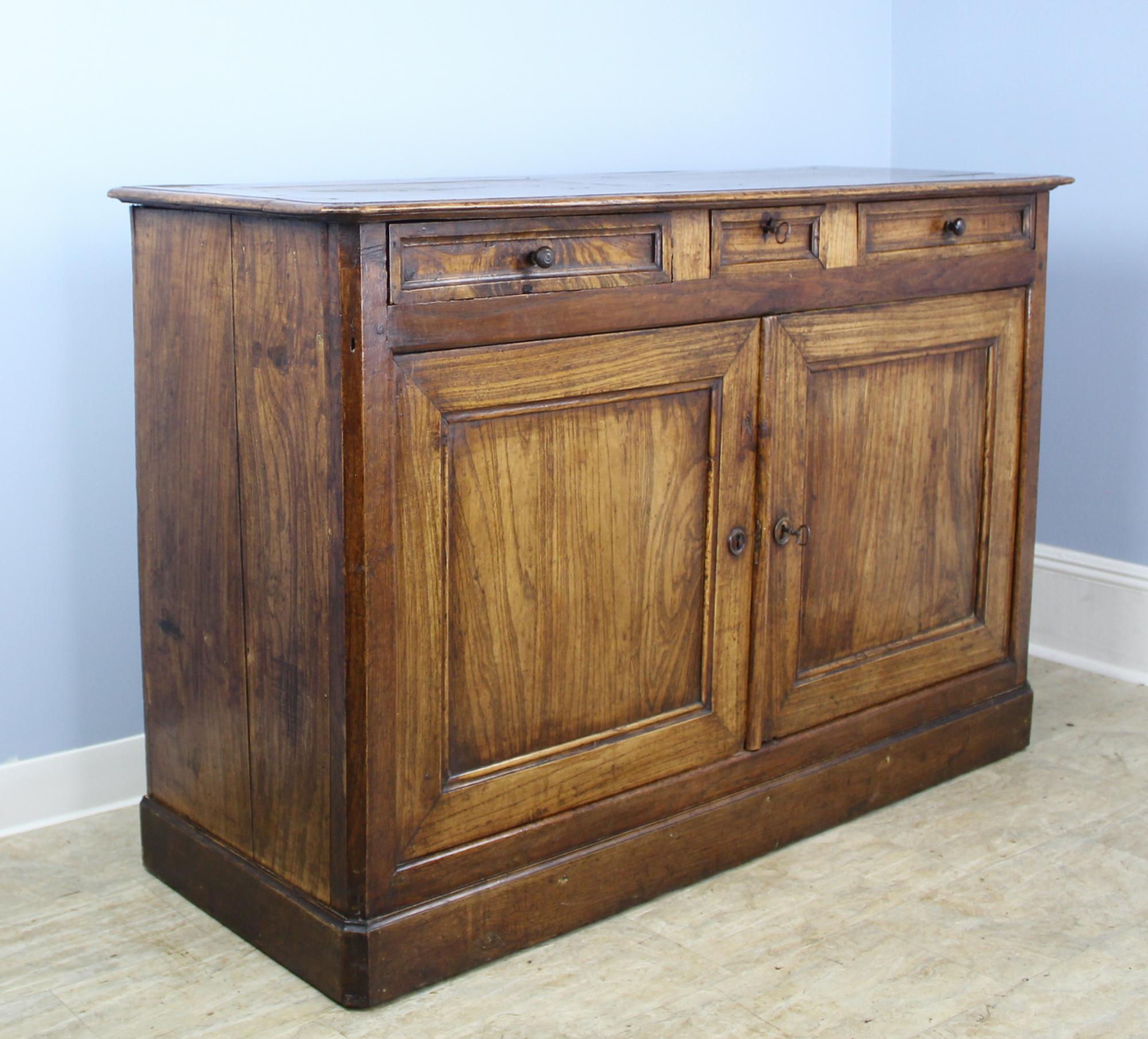 A handsome buffet in dramatically grained elm with all some Louis Philippe features, Inset panelled doors and drawers, canted corners on the top, and a simple molding at the base. The centre drawers has a sweet inlaid heart around. The keyhole.