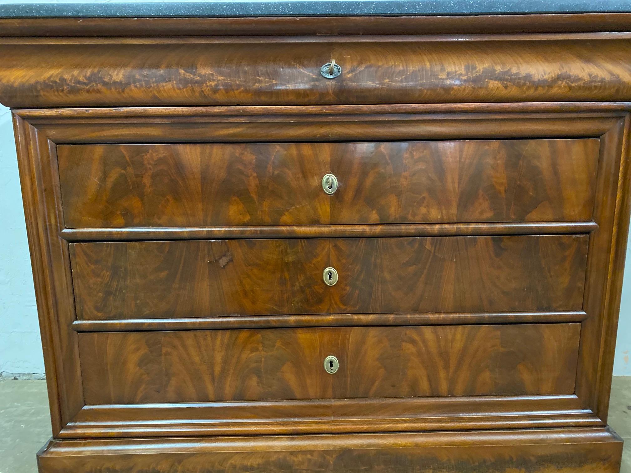 A fine 19th century Louis Philippe chest of drawers with black granite top, 4 drawers plus one hidden base drawer. This elegant and restrained Louis Philippe flame mahogany four-drawer commode, circa 1840s has book-matched veneer. The simple
