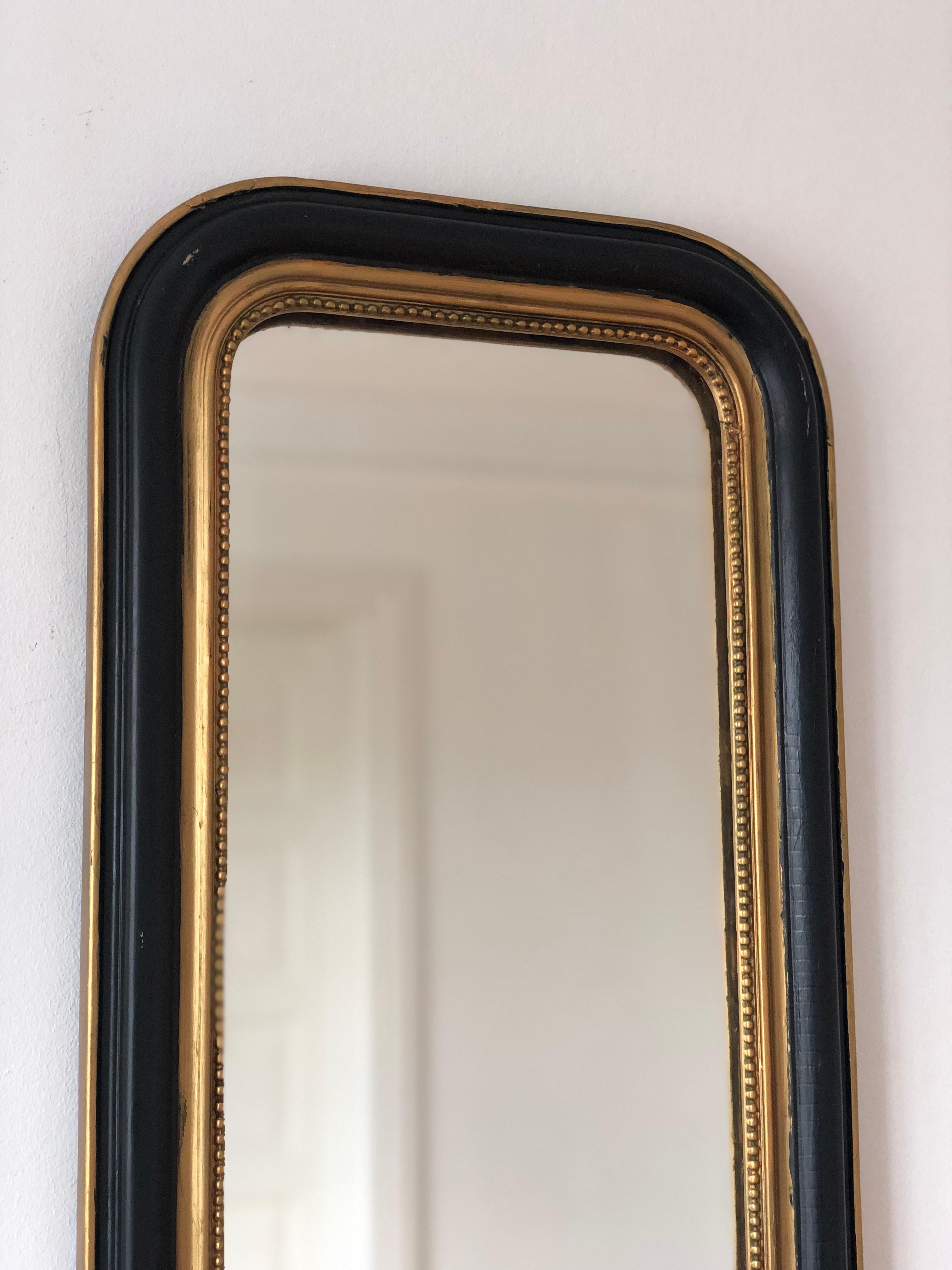 An enchanting antique Louis Philippe French mirror, dating to the late 19th century. The full length mirror features a refined black frame with a soft gold trim, a gracefully curved top and a delicate pearl rim, exuding timeless elegance and