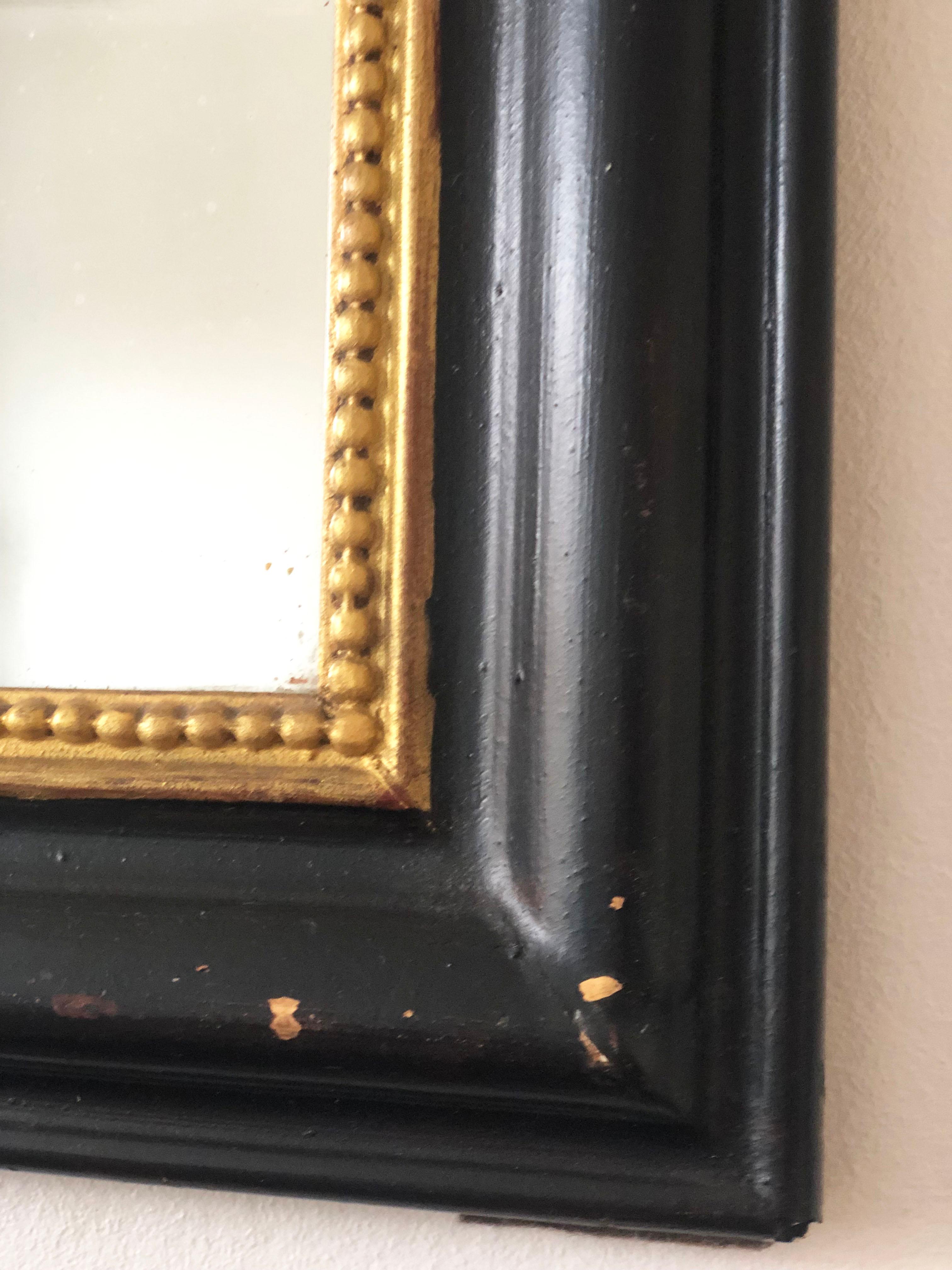 Un ravissant miroir Louis Philippe d'origine française, datant de la fin du 19e siècle.
Le miroir présente un cadre noir raffiné avec un bord en perles dorées, un verre au mercure et un dessus gracieusement incurvé, dégageant une élégance et un