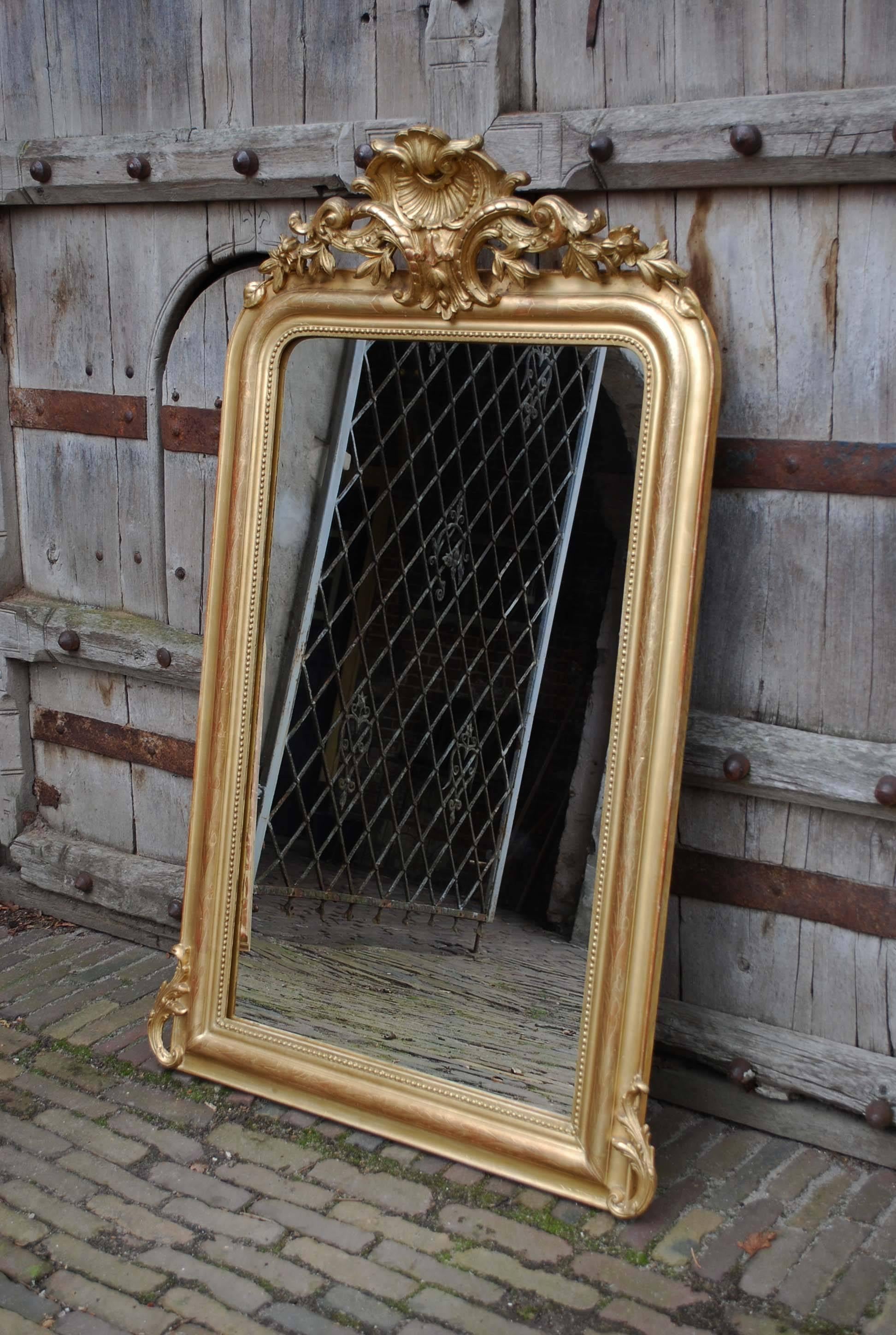A Louis Philippe style gold leaf gilt frame with original mirror glass.
The mirror has an ornate crest with a central scallop shell surrounded by classical and floral elements.
The elevated part of the frame has a floral engraving and this part